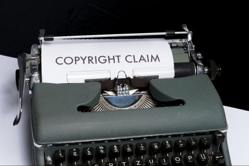 A typewriter with a piece of paper reading “COPYRIGHT CLAIM” in large letters sticking out of the top.