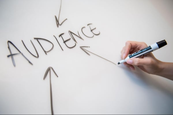 A hand drawing an arrow towards the word “Audience” on a whiteboard.