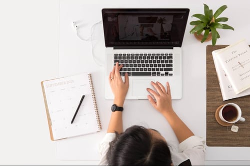 a young person using a laptop with various items on their desk. 