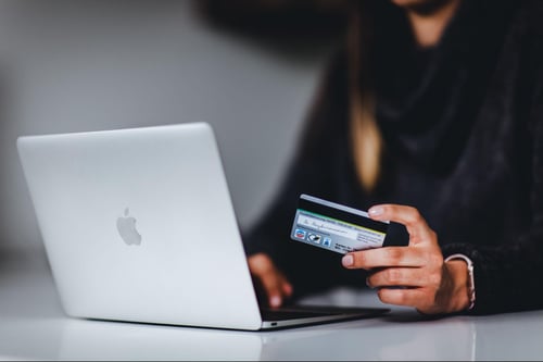 A person using an Apple laptop while holding a credit card. 