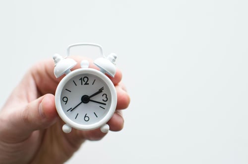 A hand holding a small white alarm classic alarm clock