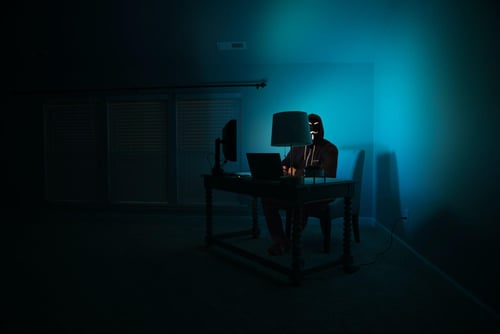 Hacker in mask sitting at a computer in the dark