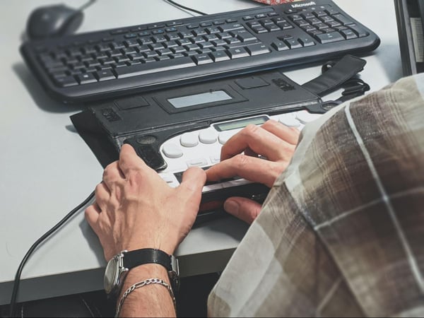 A person using a computer with the aid of an adaptive tool.