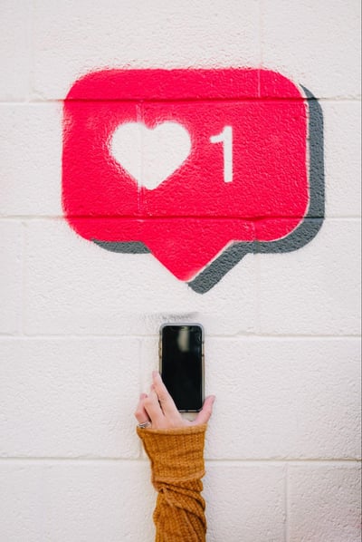 A person holding their smartphone under a mural of an Instagram like notification