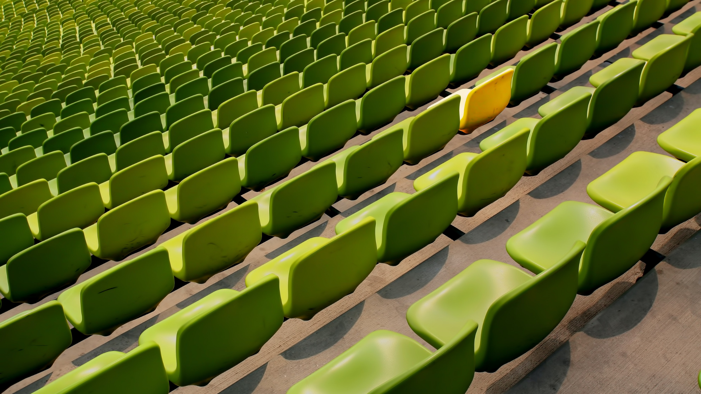Rows of green stadium seats with one yellow seat