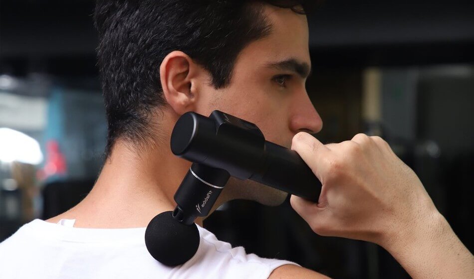 A white man with dark hair uses a massage gun