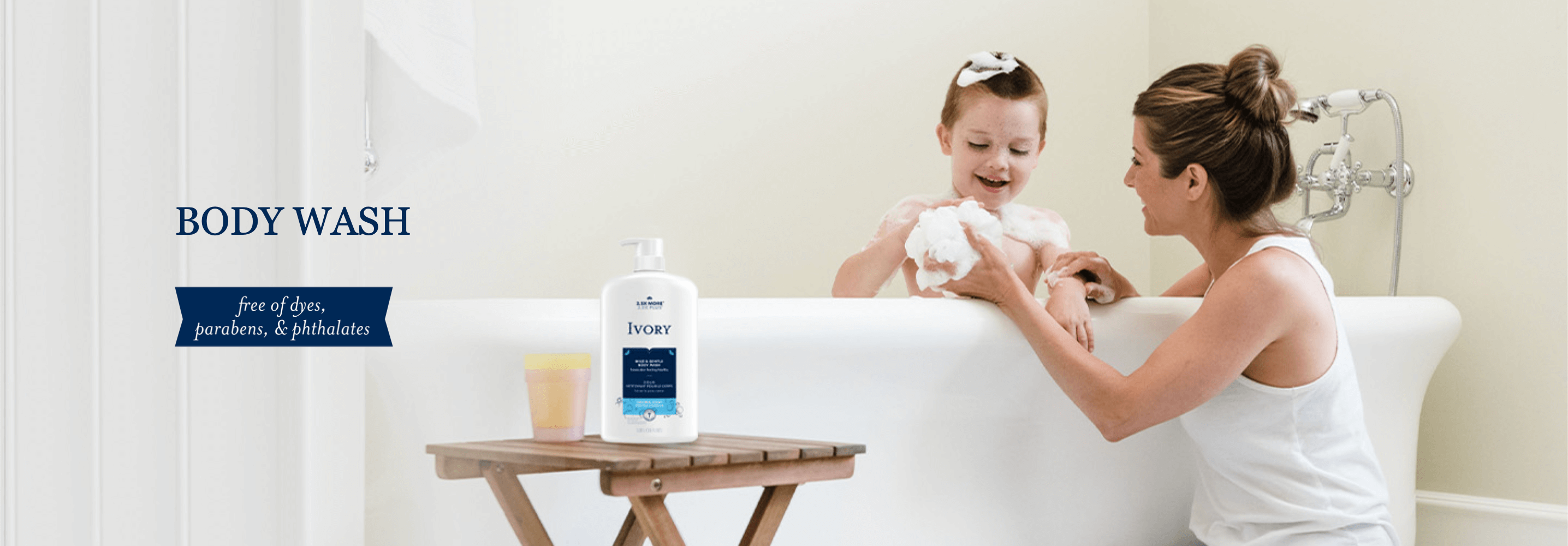 A bottle of body wash next to a cup on a little folding table next to a bathtub. 