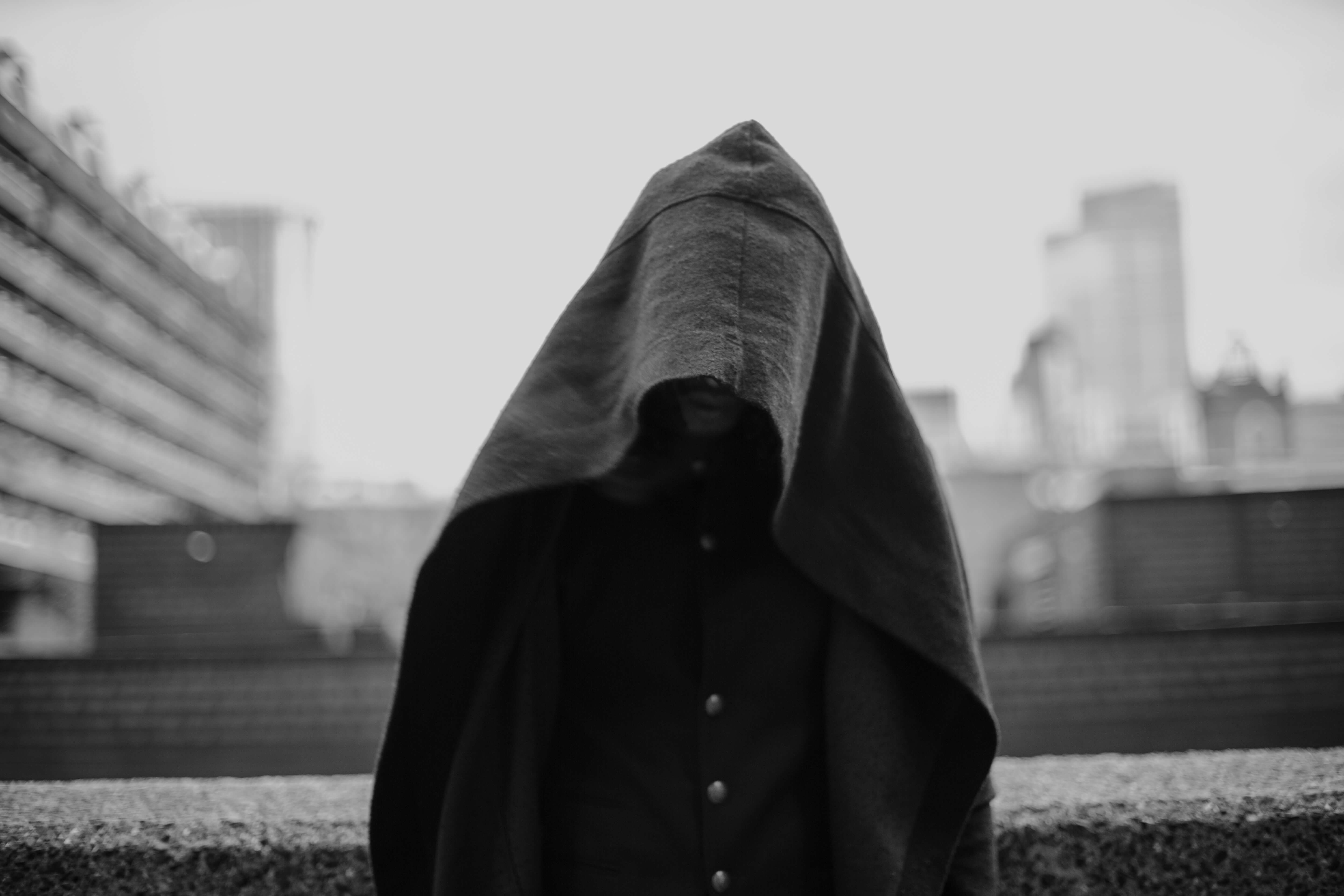 A black and white photo of a person covering their face with a cloak