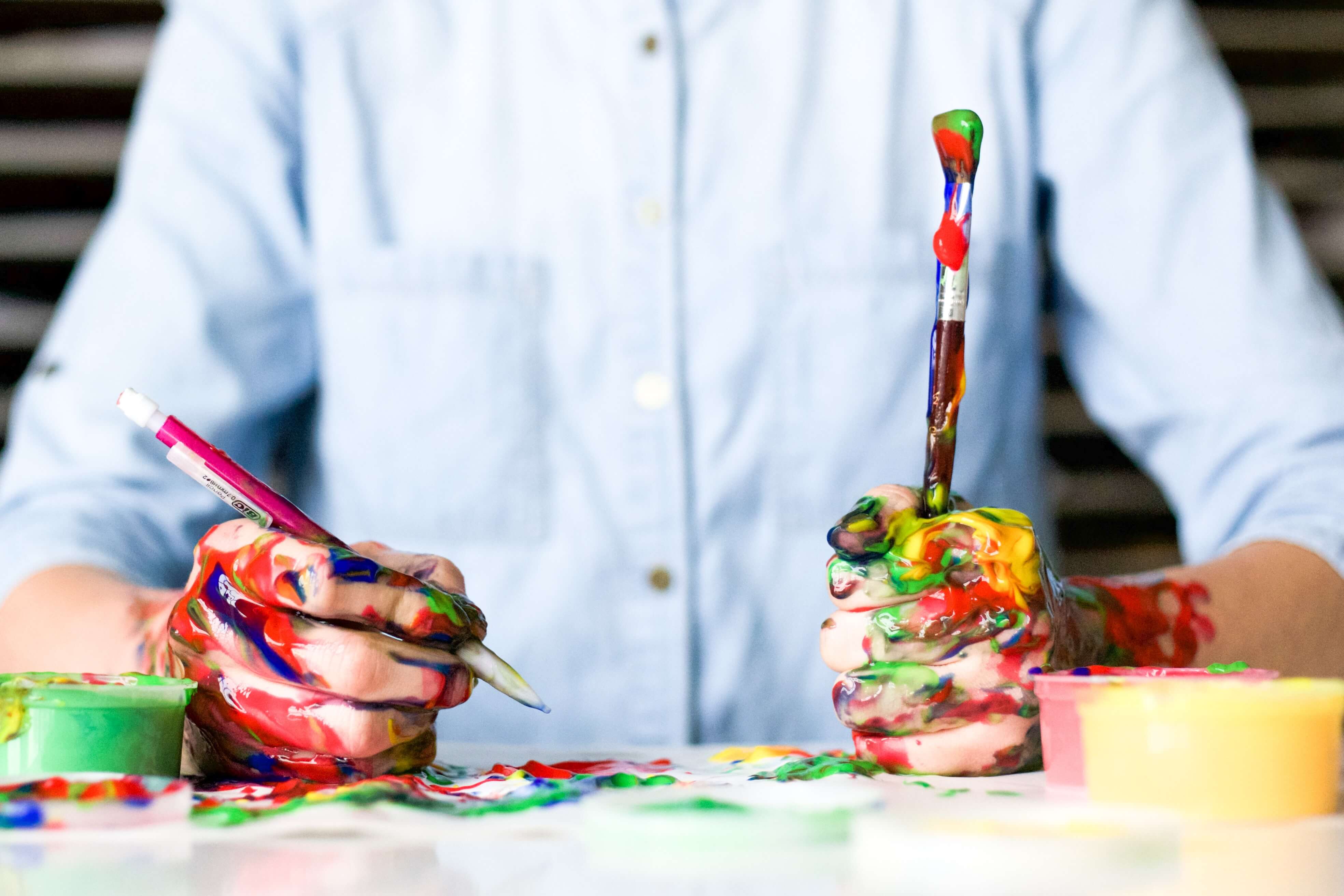 An artist with their hands covered in different colors of paint