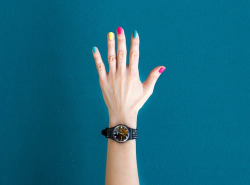 Hand raised with multicolored nails and a black watch