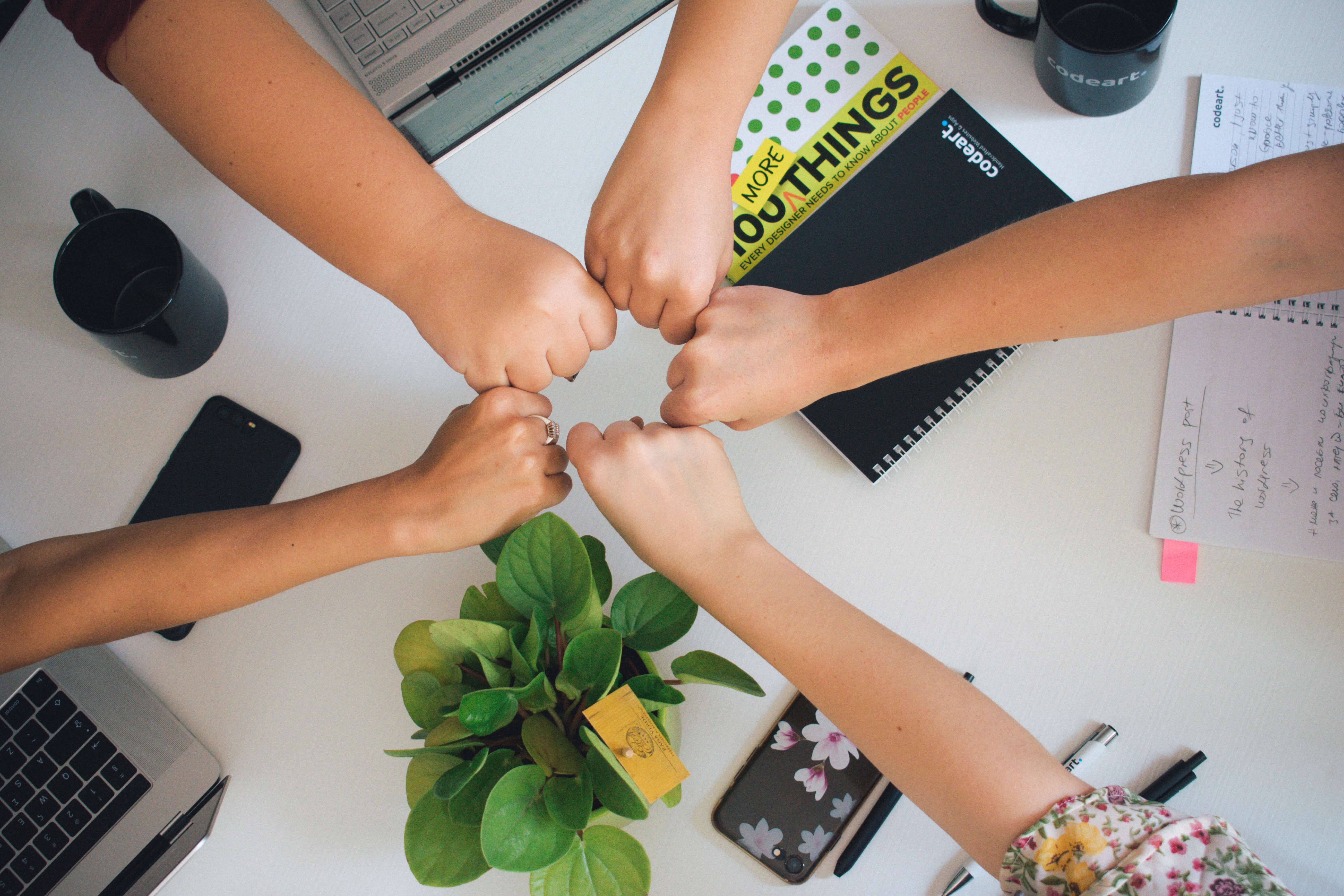 Five people fist bumping over a shared table at an office