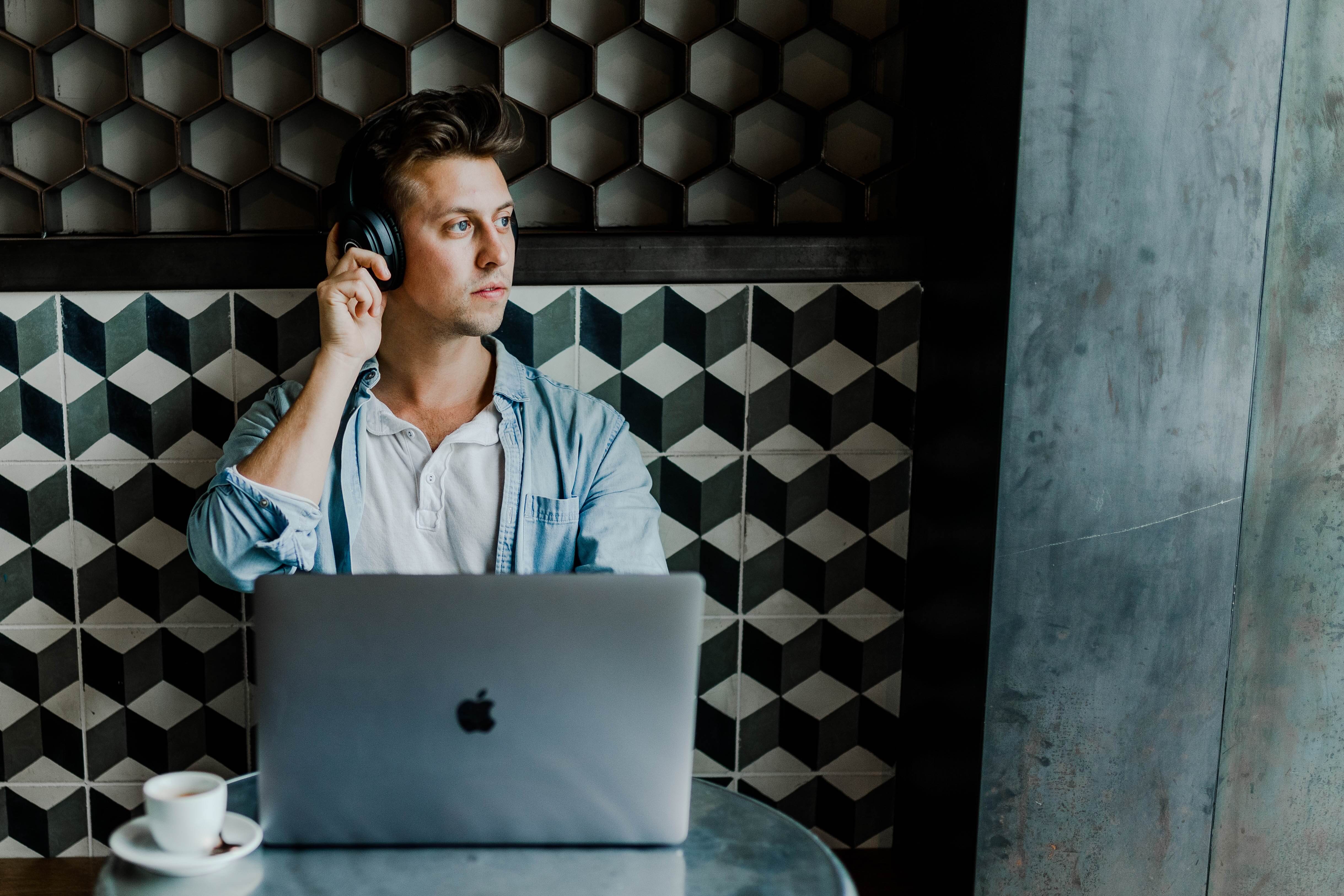 A white man uses a laptop with headphones on while sitting at a cafe