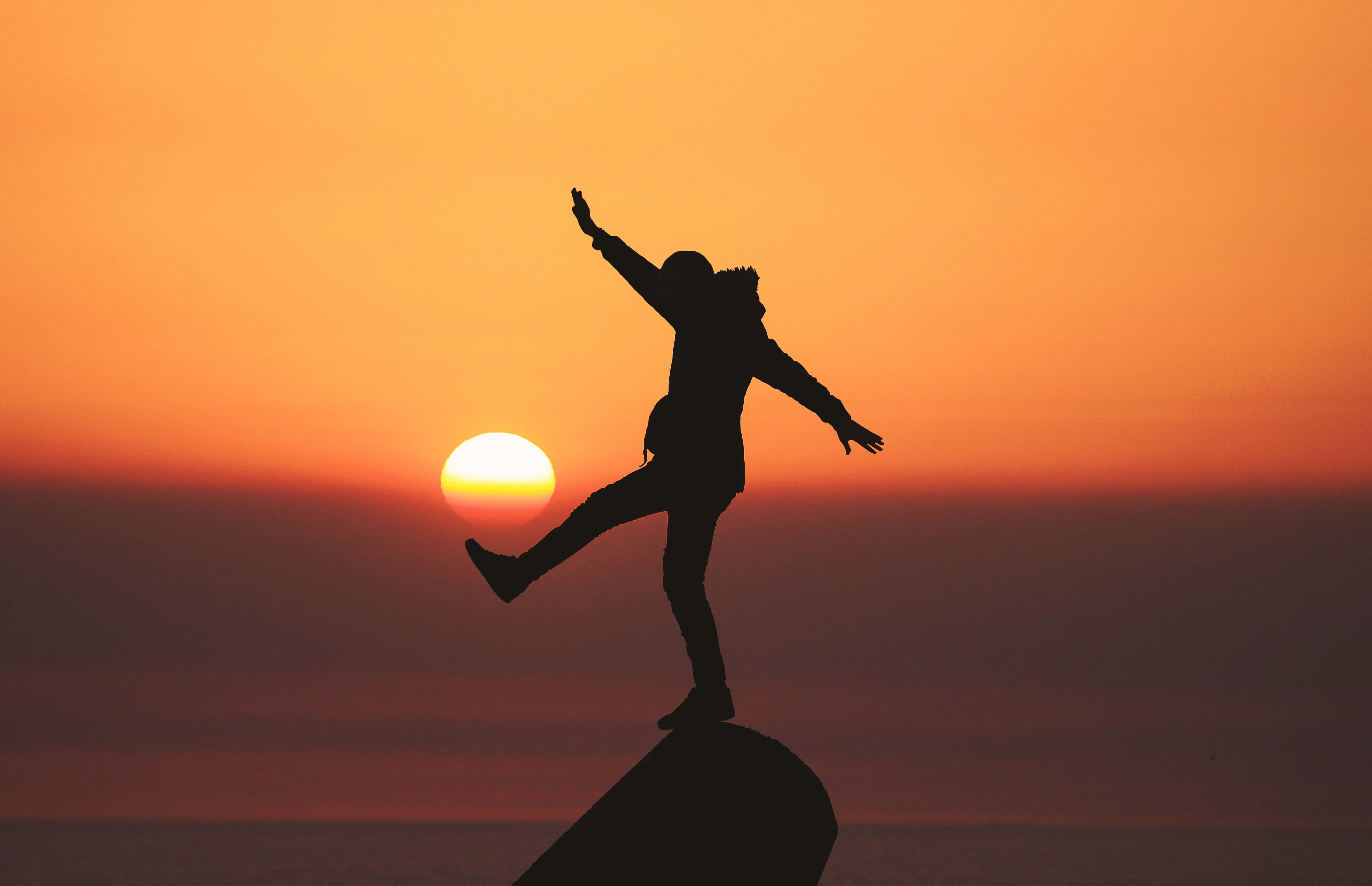 A silhouette of a person balancing on a rock at sunset