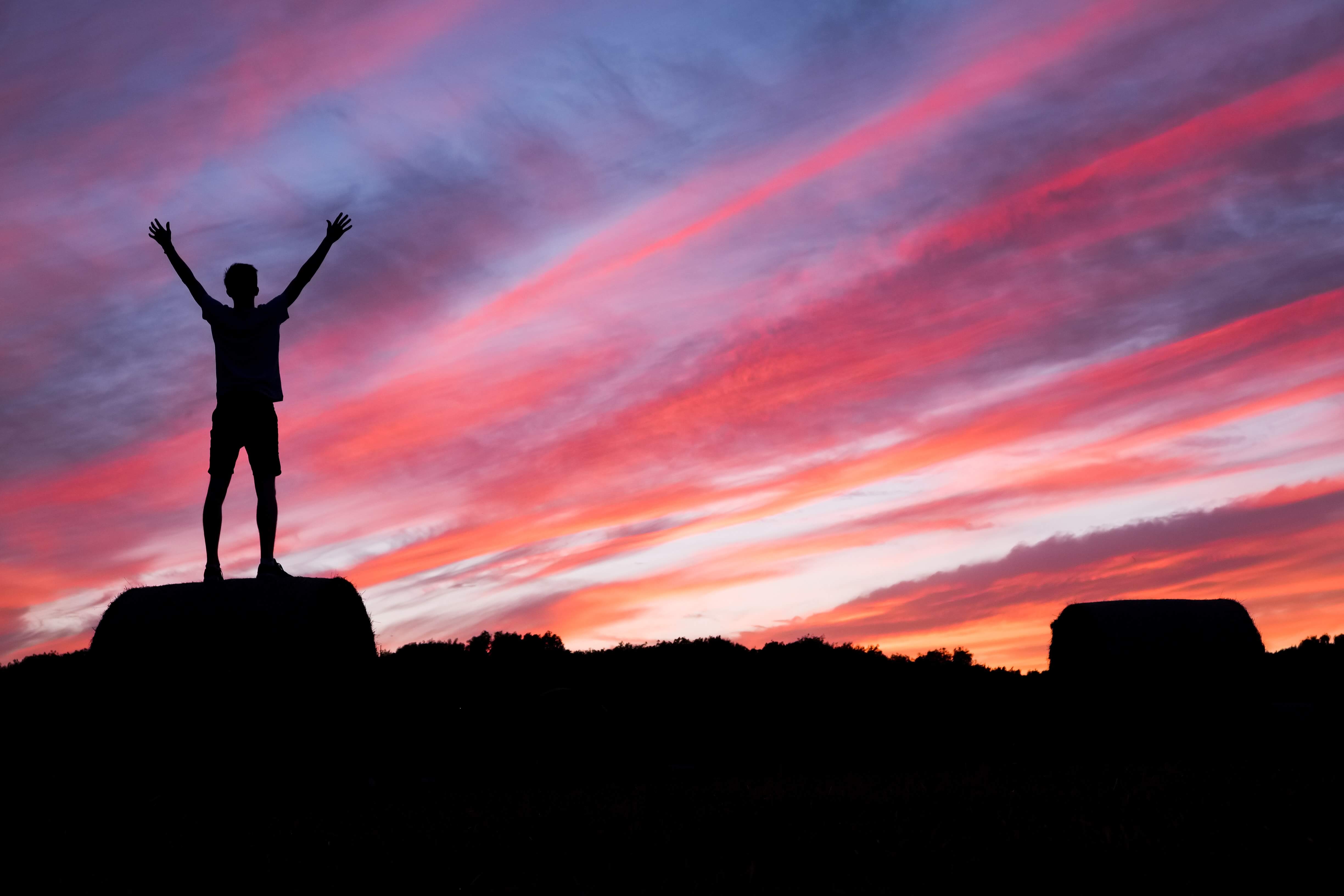 A person celebrating on top of a mountain at sunset