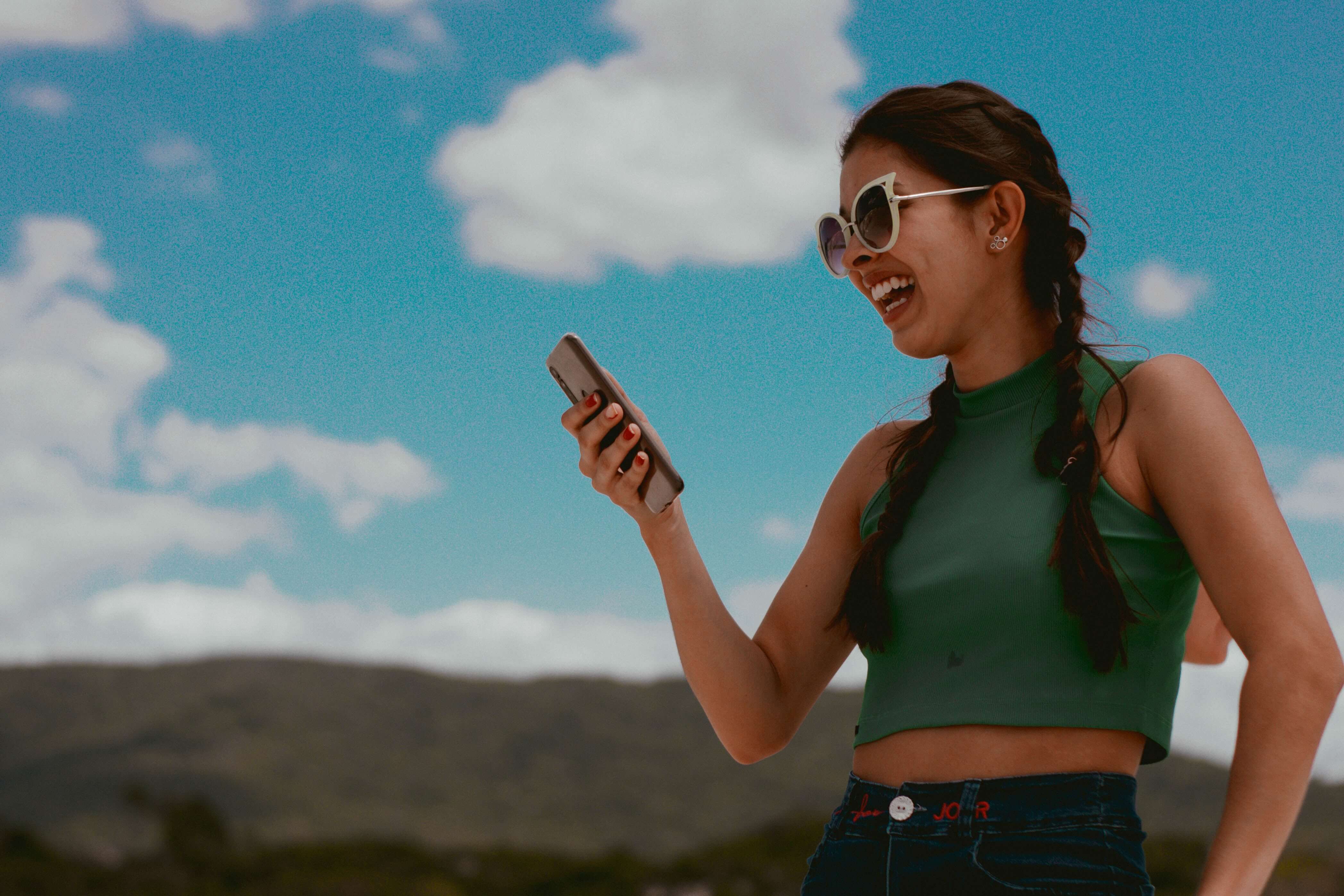 A young ethnically ambiguous woman smiles with an open mouth as she looks at her phone