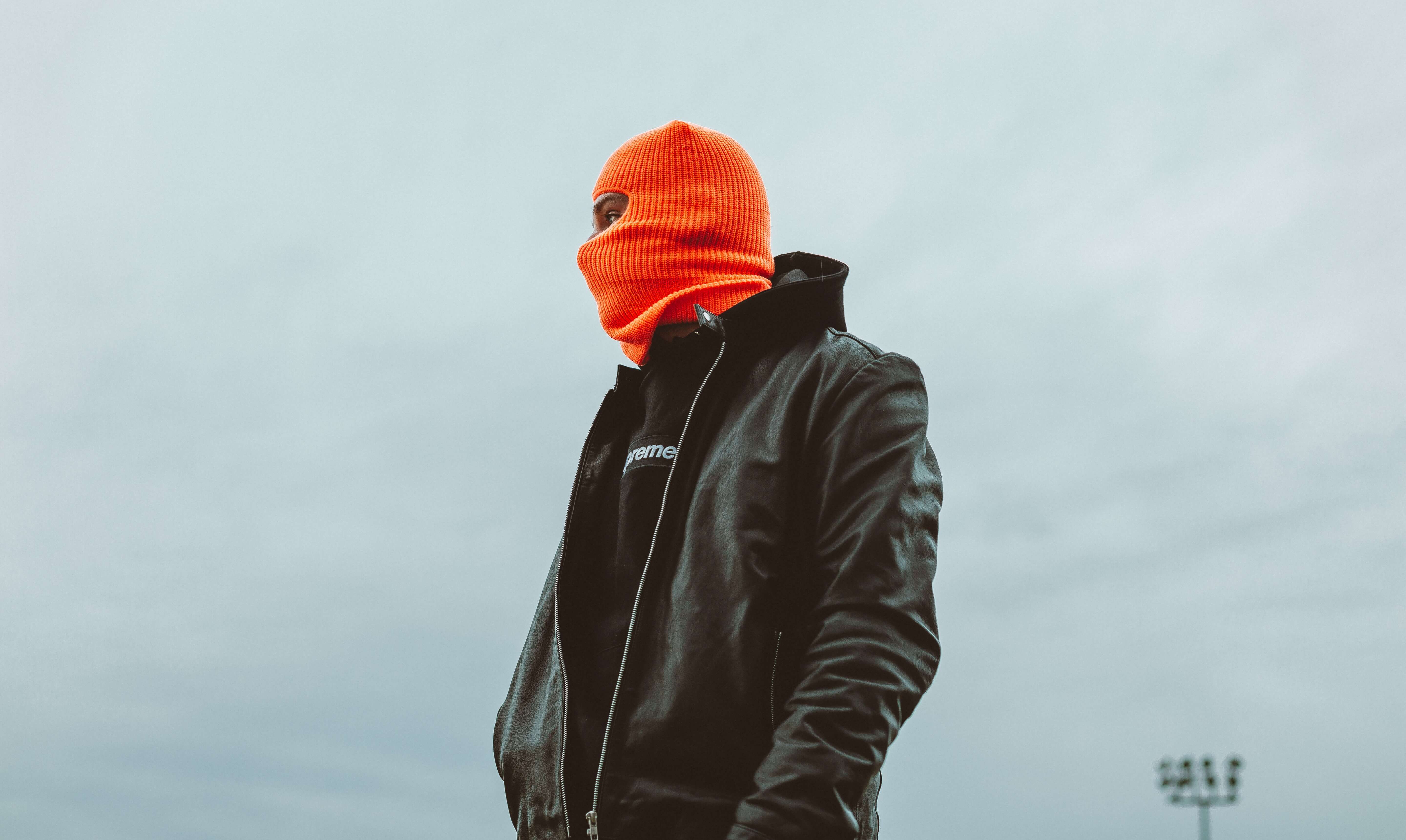 A black man wearing an orange balaclava and a leather jacket