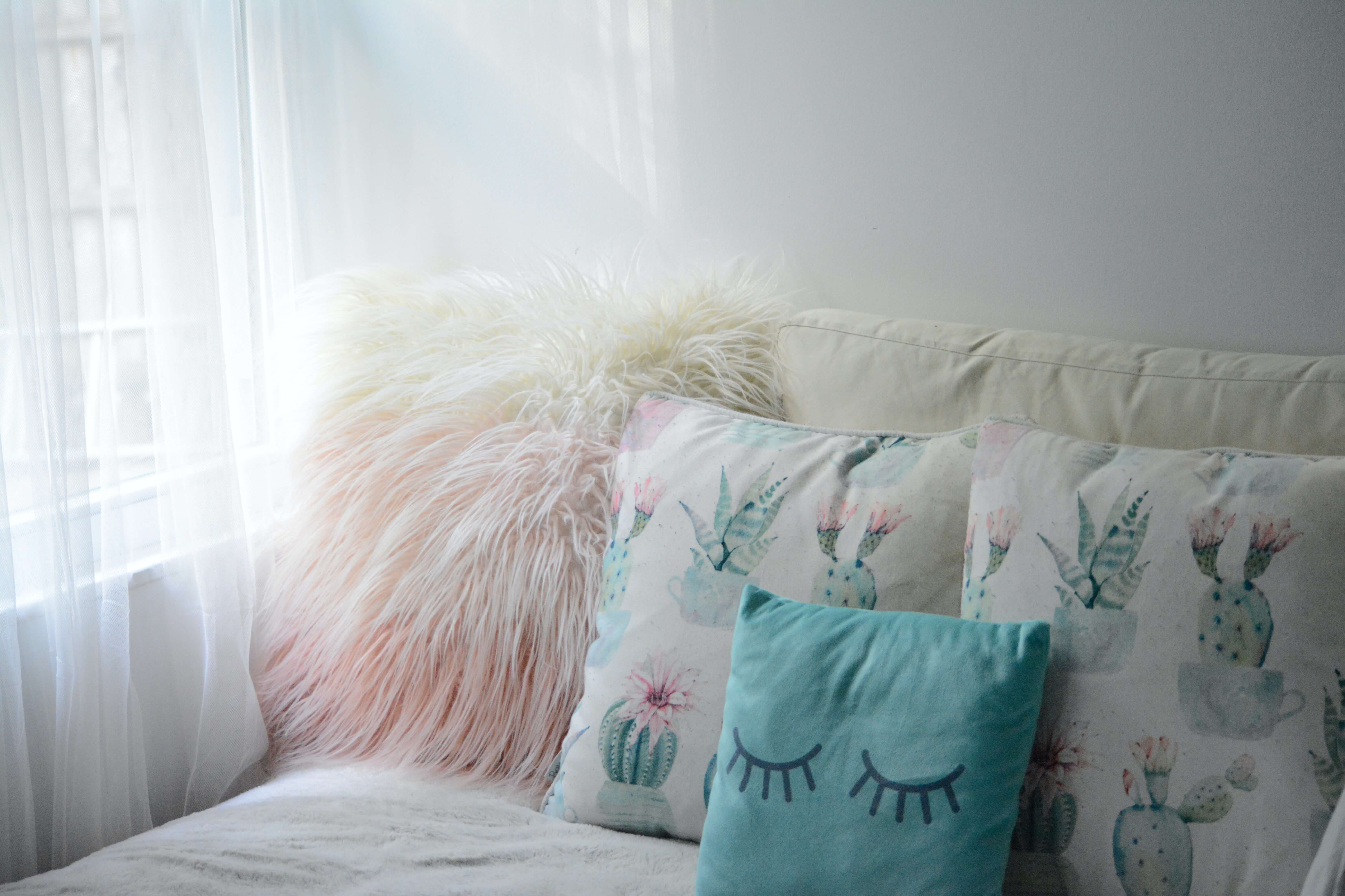 Three throw pillows on a couch. One has eyes printed on it and the other two have paintings of cactuses