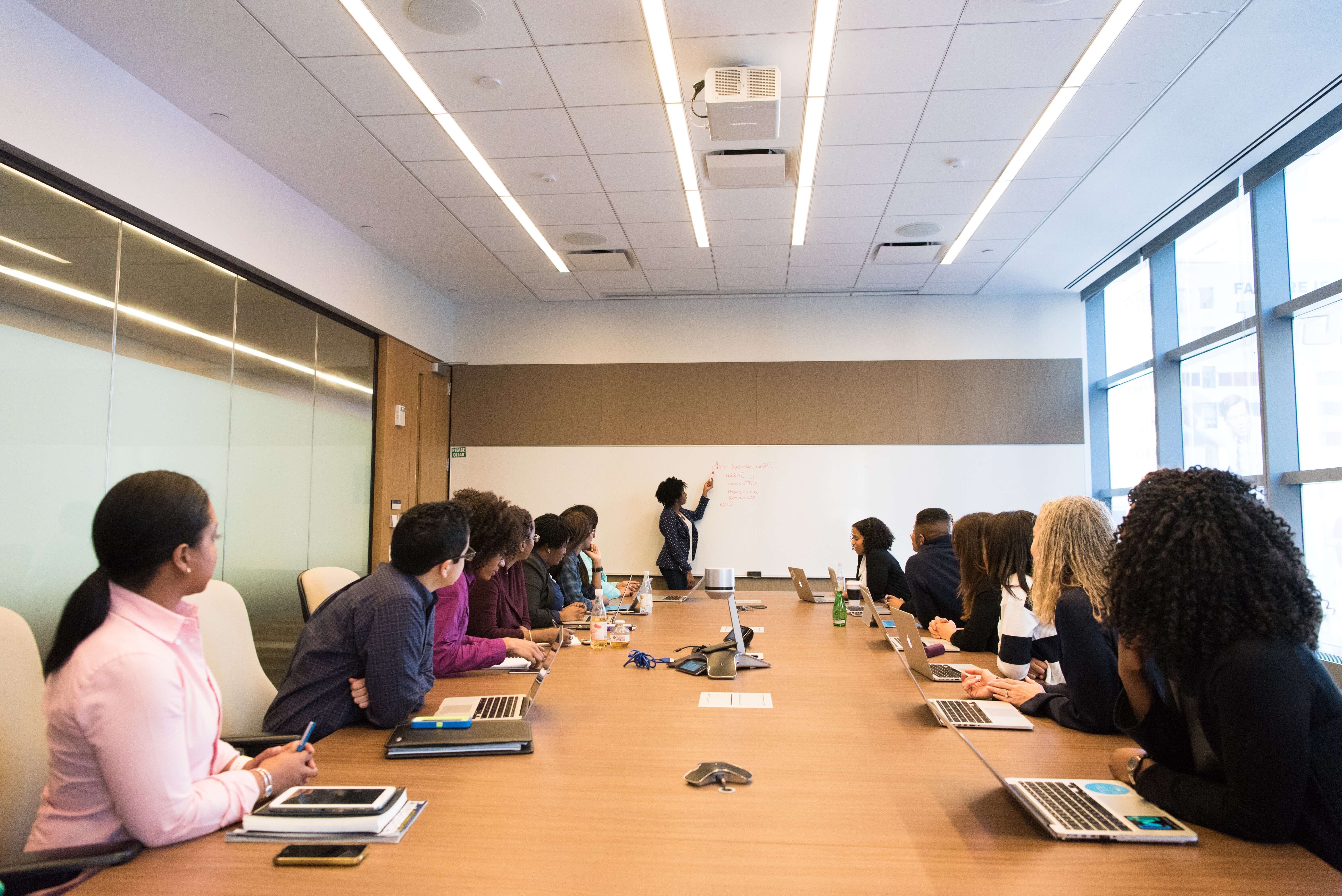 A black woman writing on a whiteboard in front of a business meeting