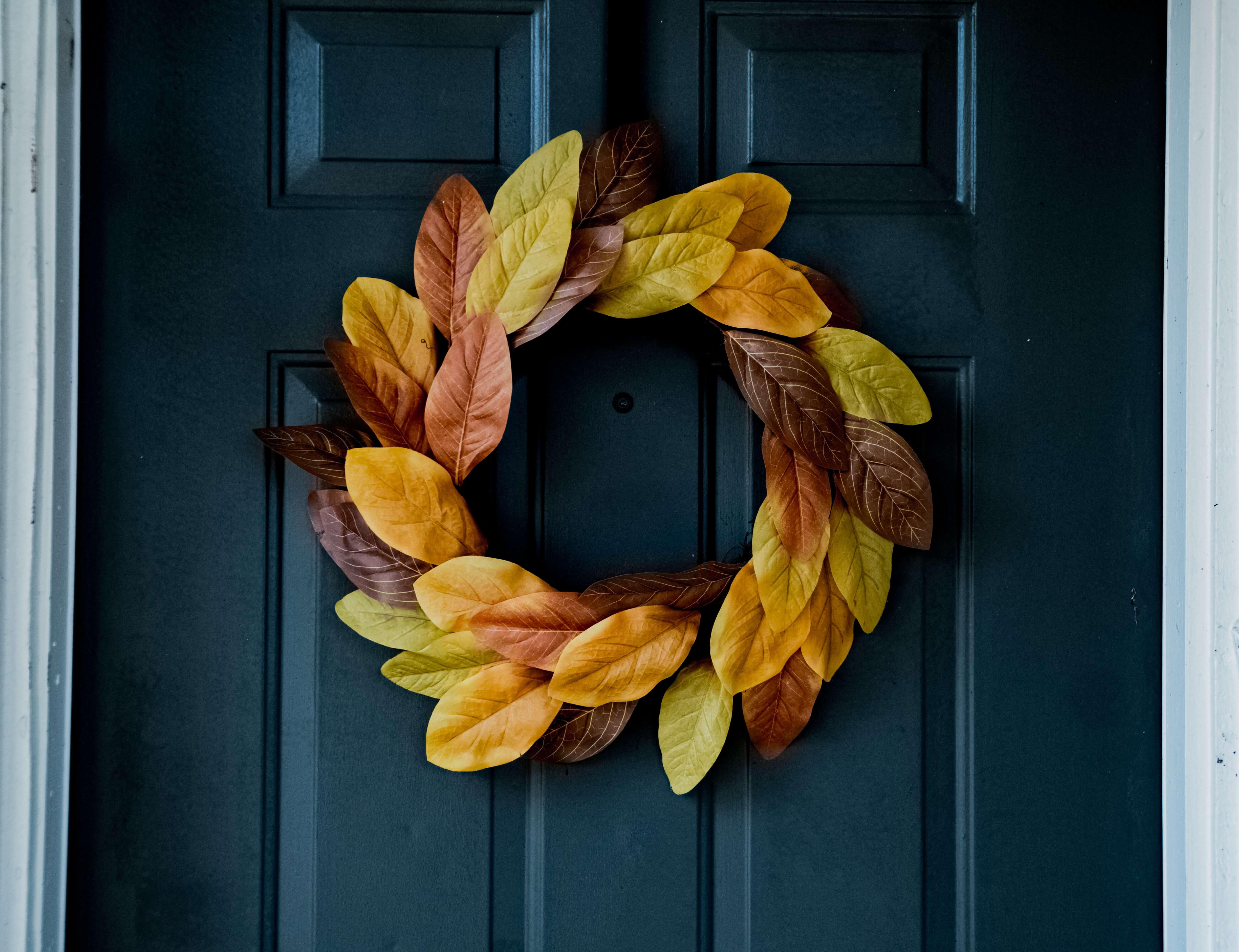 A wreath made of artificial fall leaves hanging on a front door