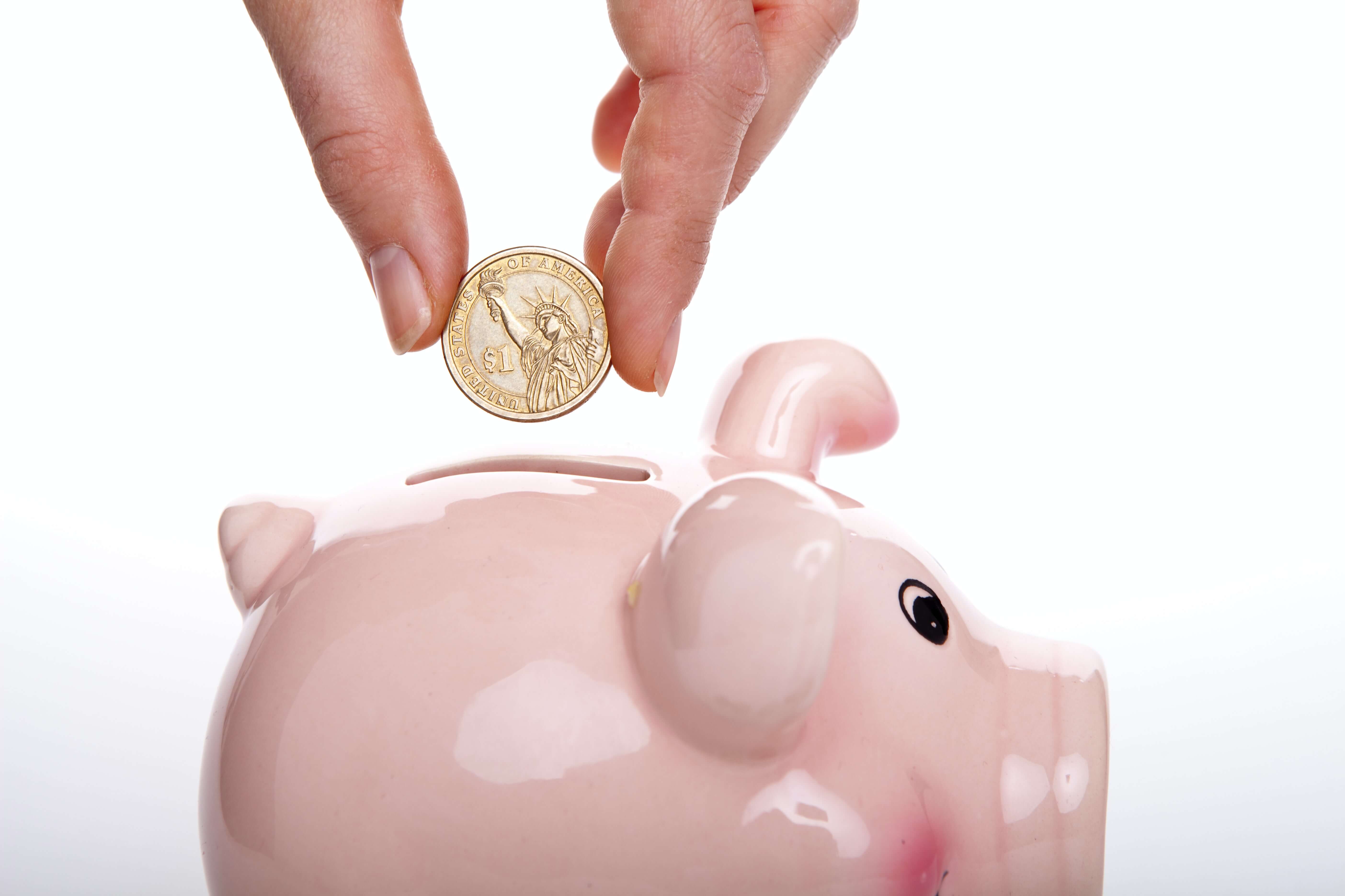 A closeup of a hand dropping a coin into a piggy bank