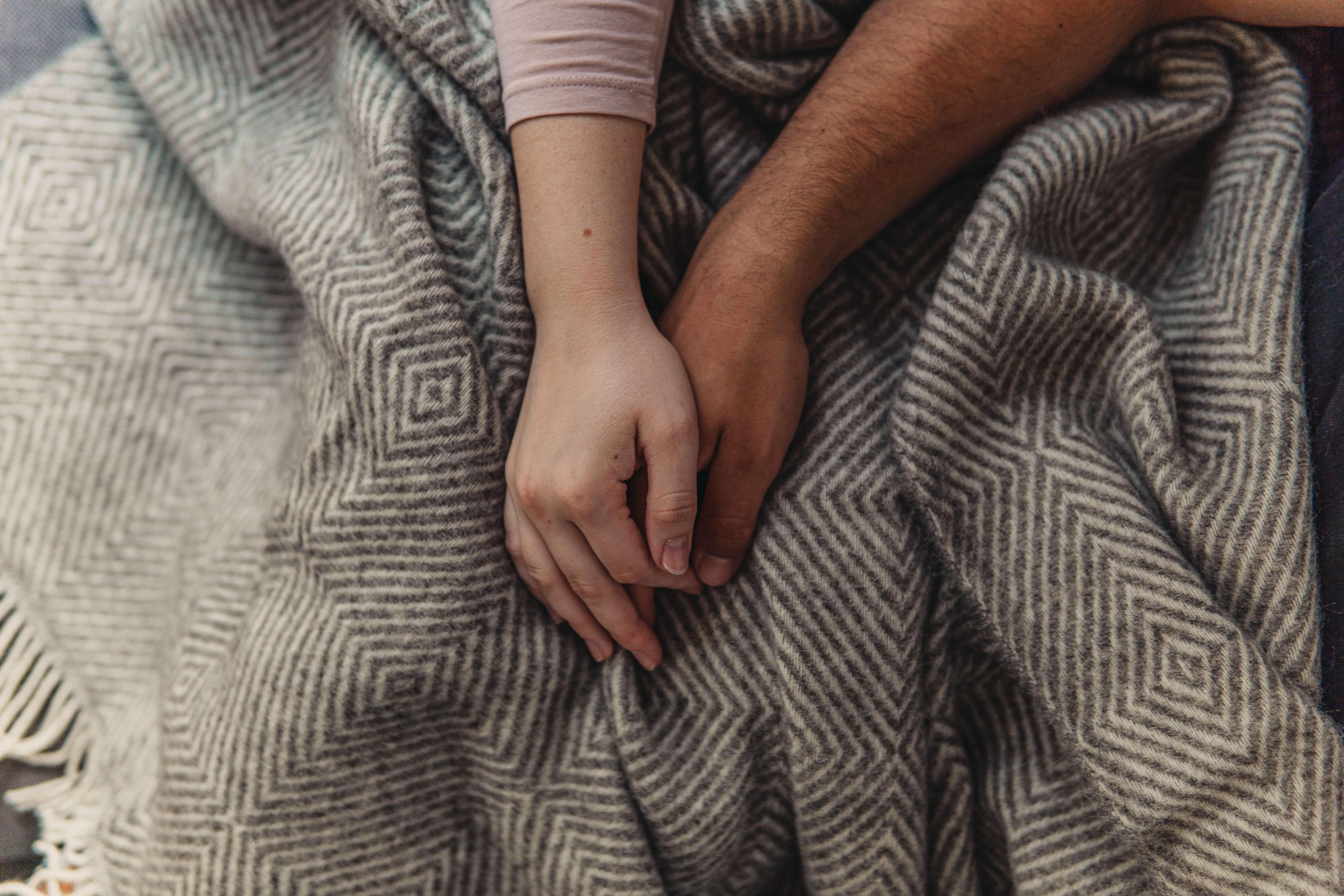 Two people holding hands over a blanket