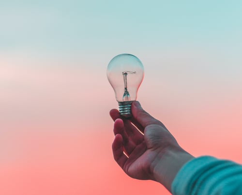 A hand holding a lightbulb up against the sunset