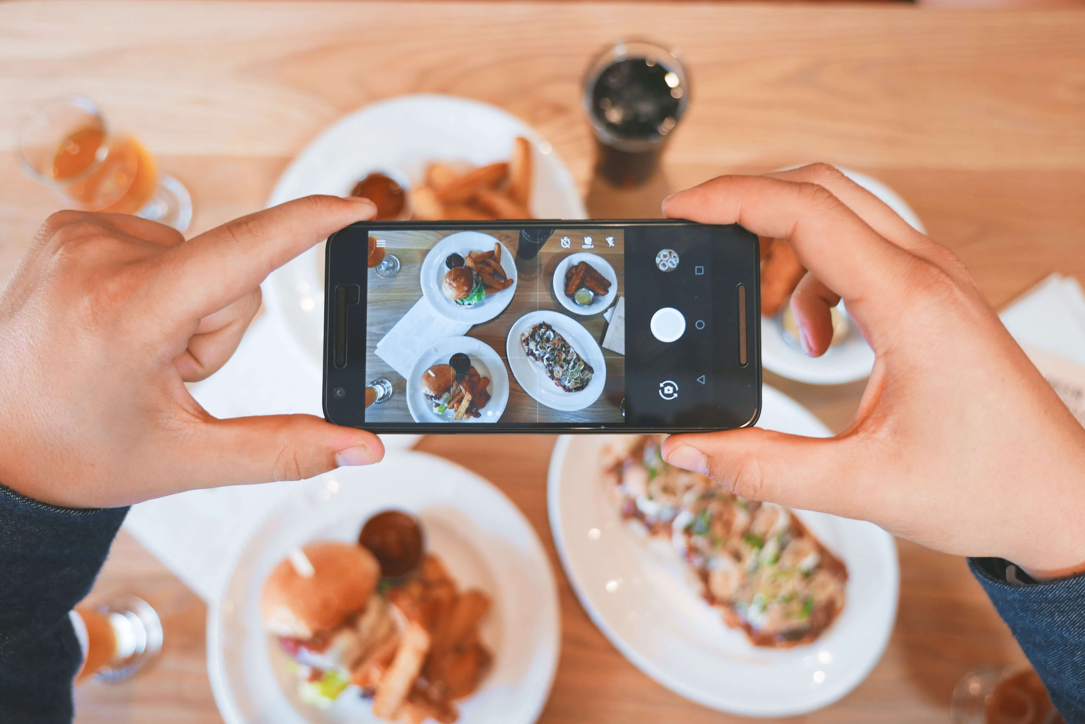 A person takes a photo with their phone of four small plates of food