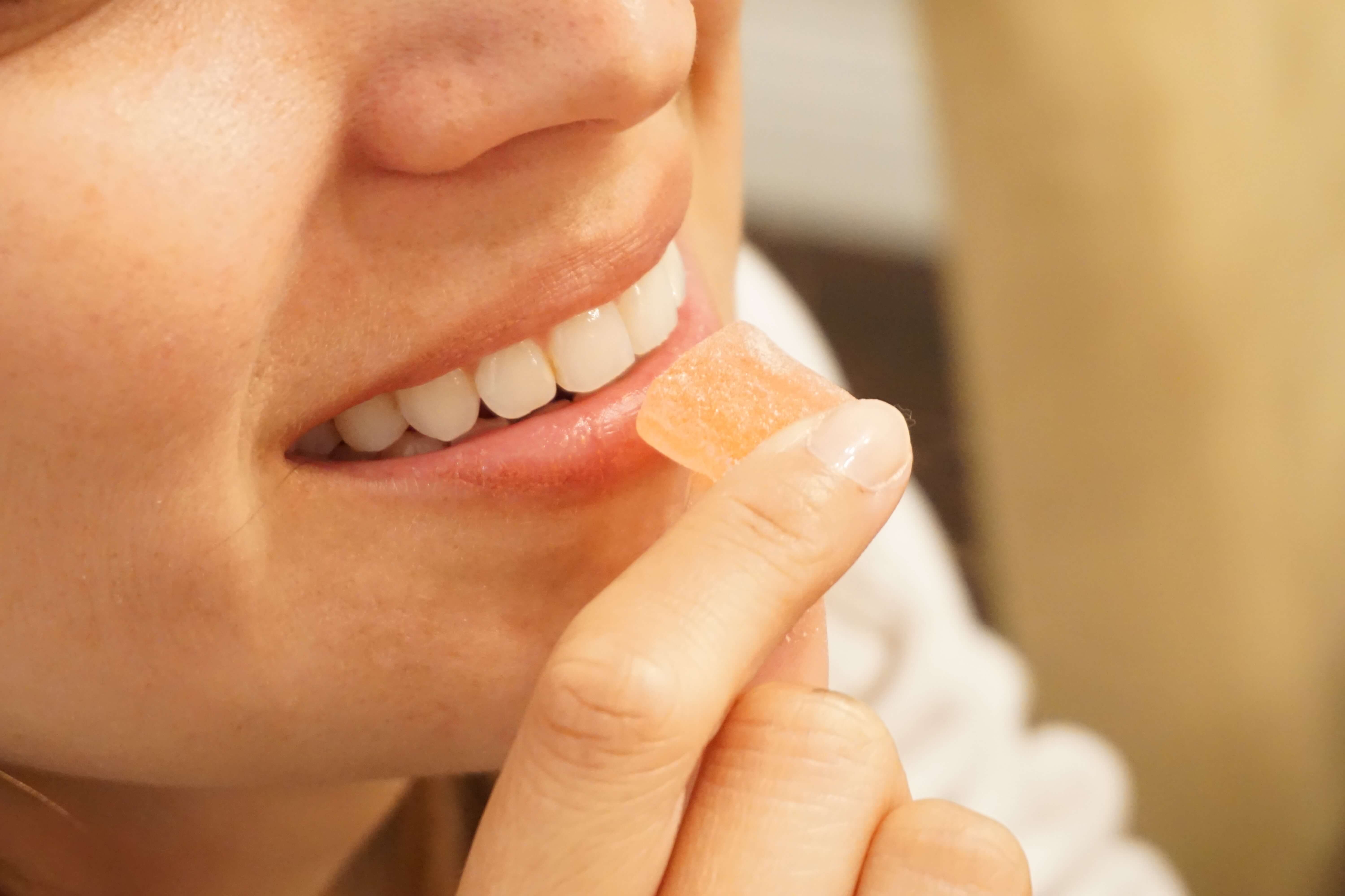 A closeup of a person holding a gummy vitamin to their mouth