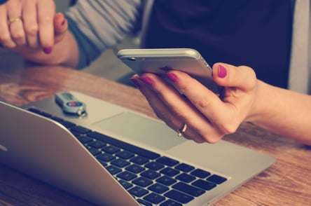 female hands holding a cell phone and checking a computer.