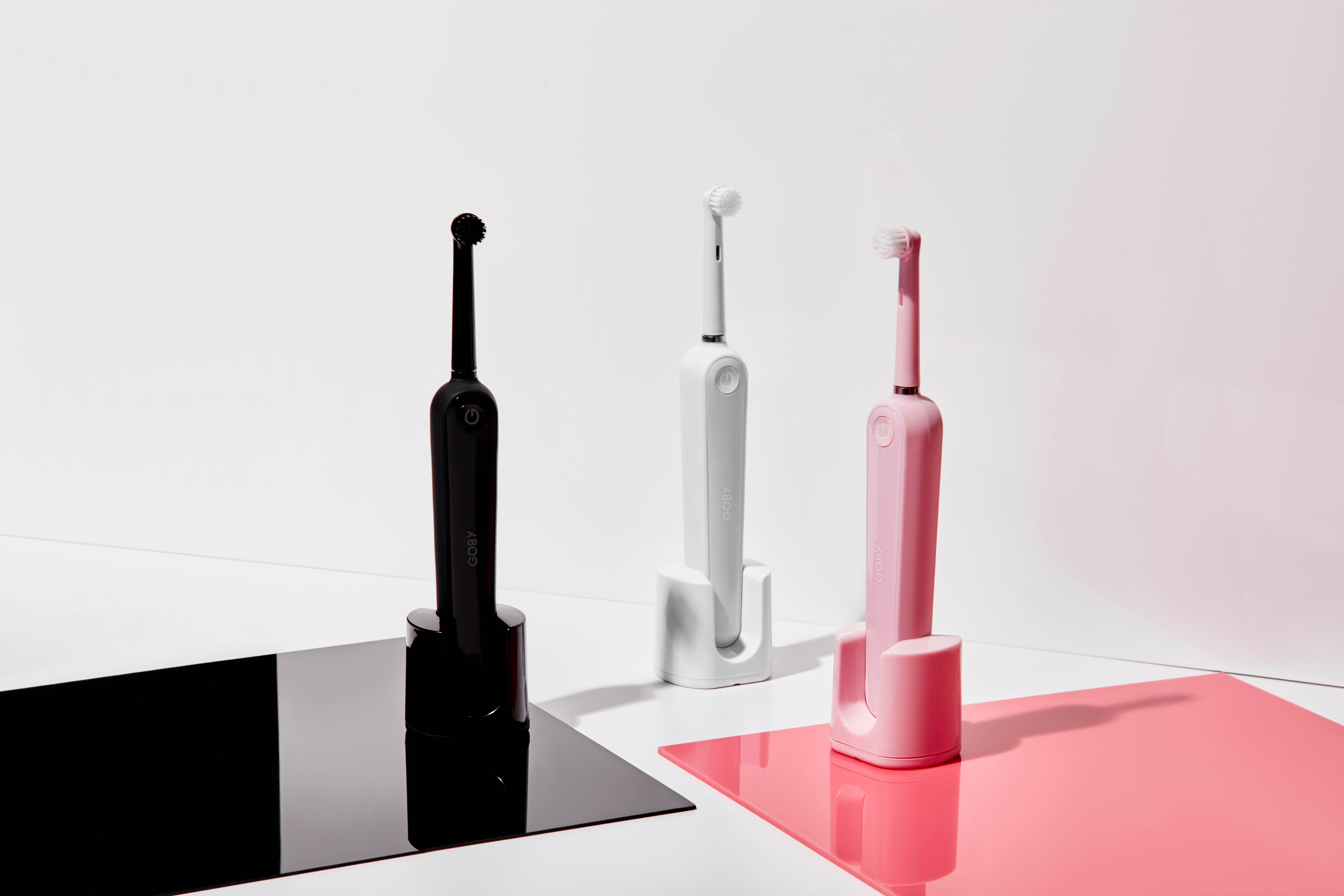 Three electric toothbrushes: one black, one white, and one pink