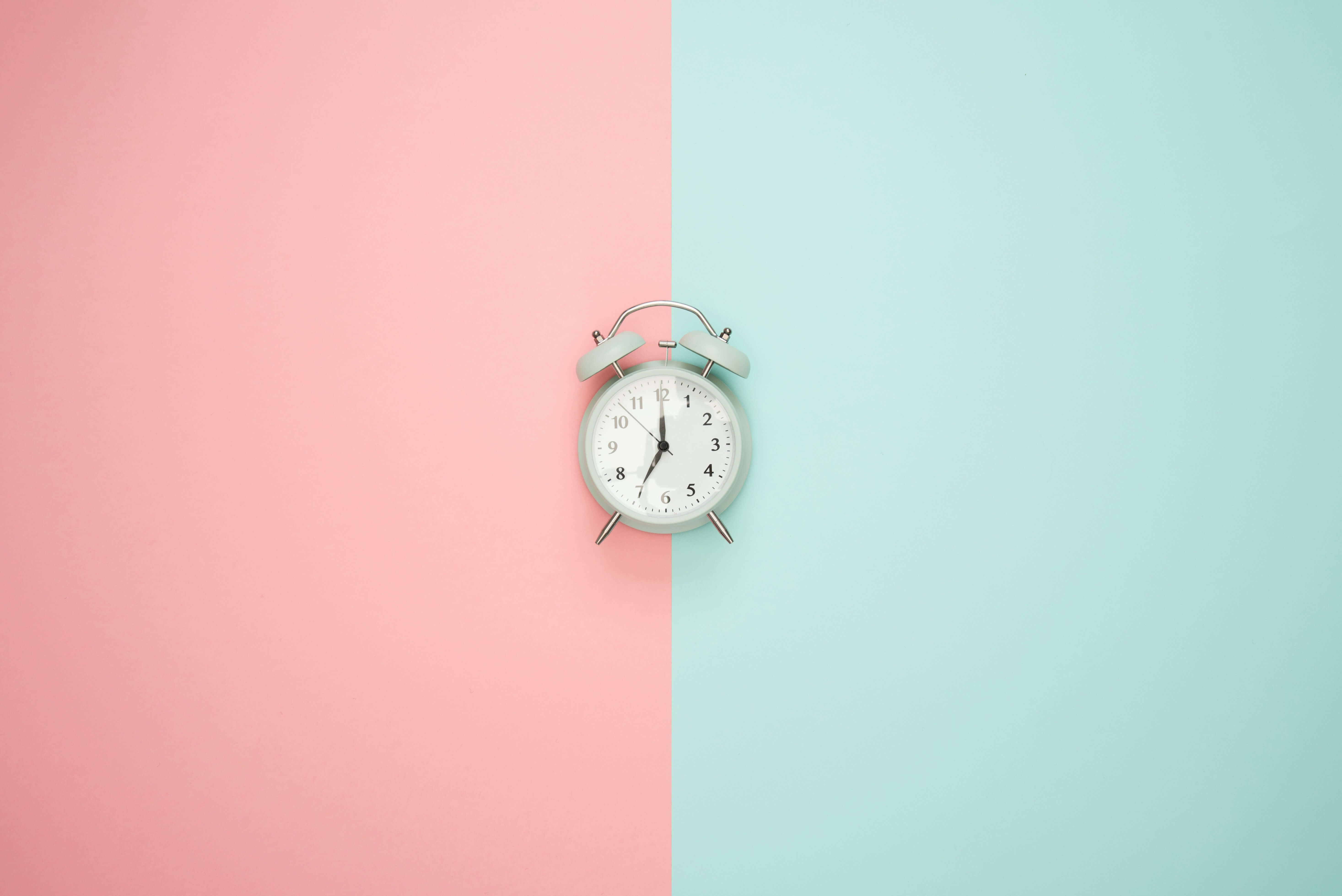 An old-style alarm clock in the center of a half pink and half blue background