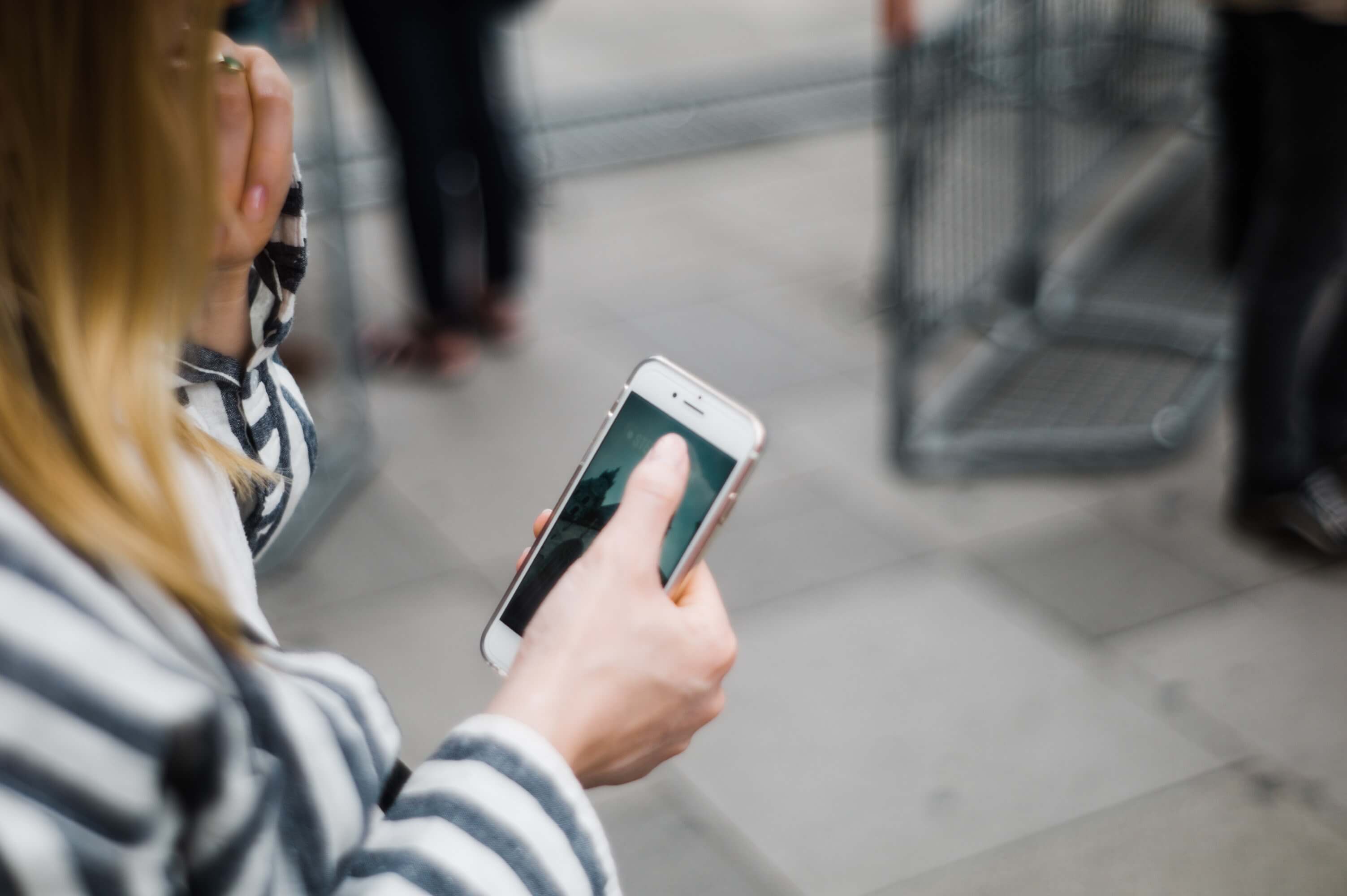 A woman using an iPhone while standing on a sidewalk