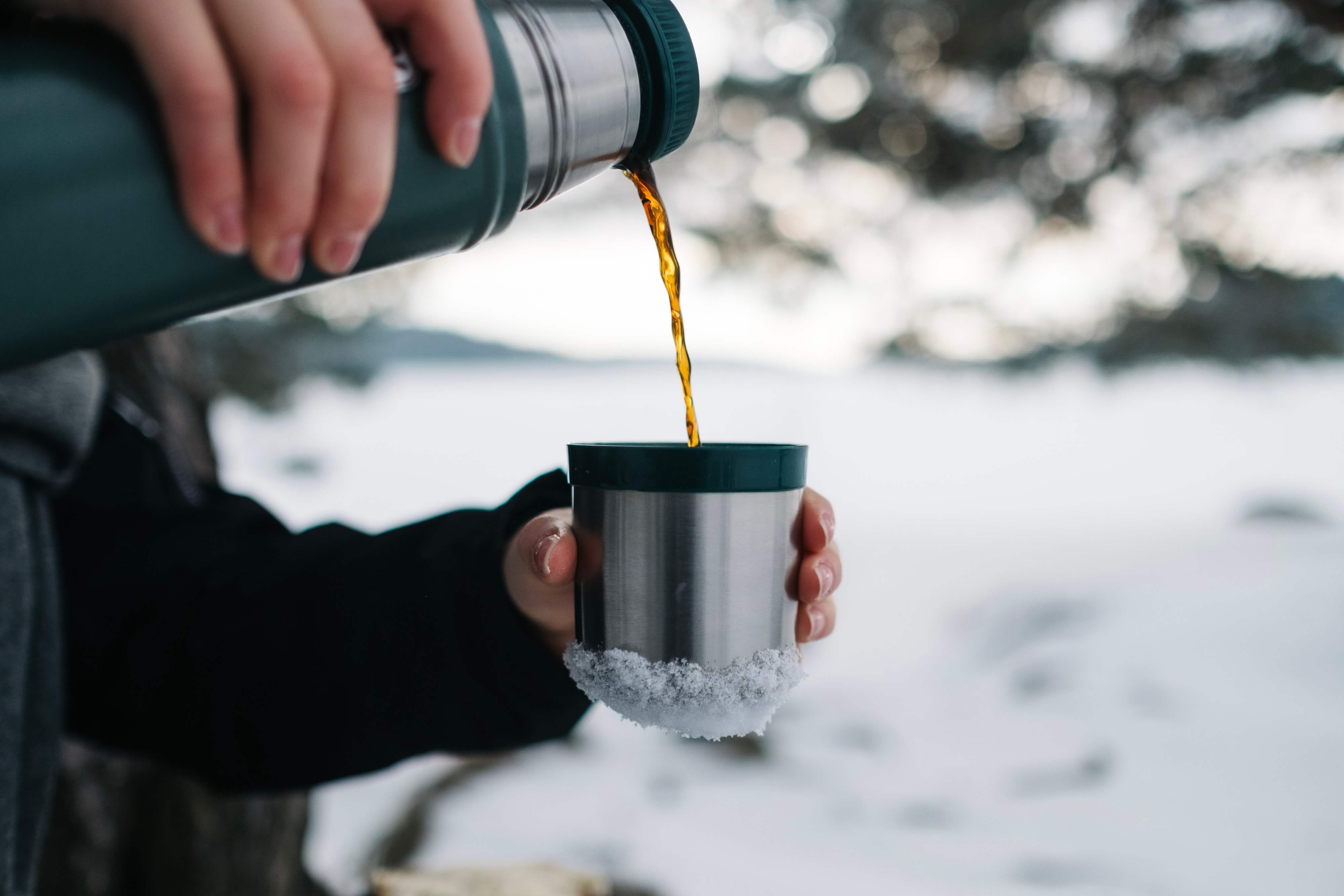 A person pours coffee from a thermos into the cap