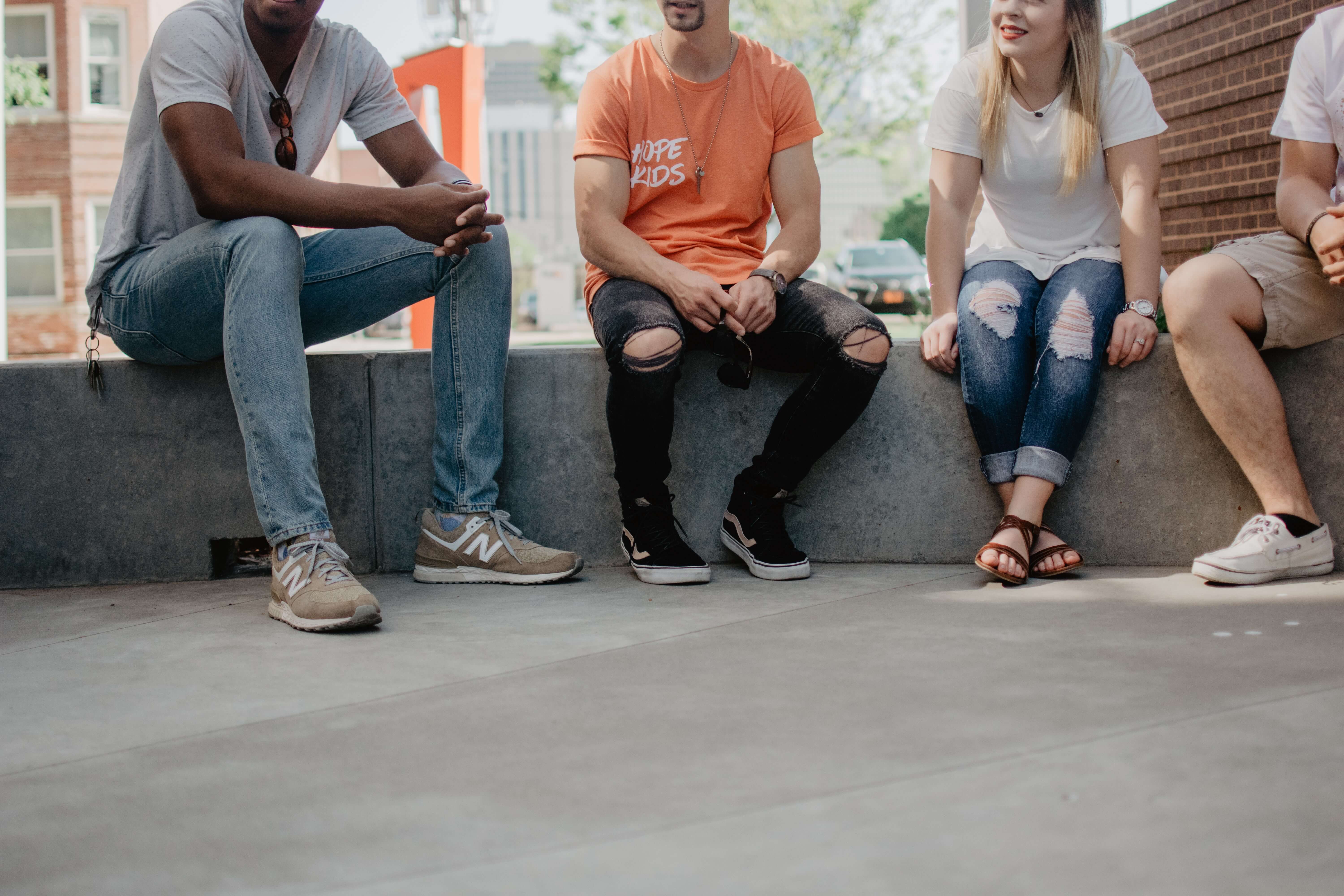 A black man, a Middle Eastern man, a white woman, and a white man in casual clothing sit together on a concrete bench