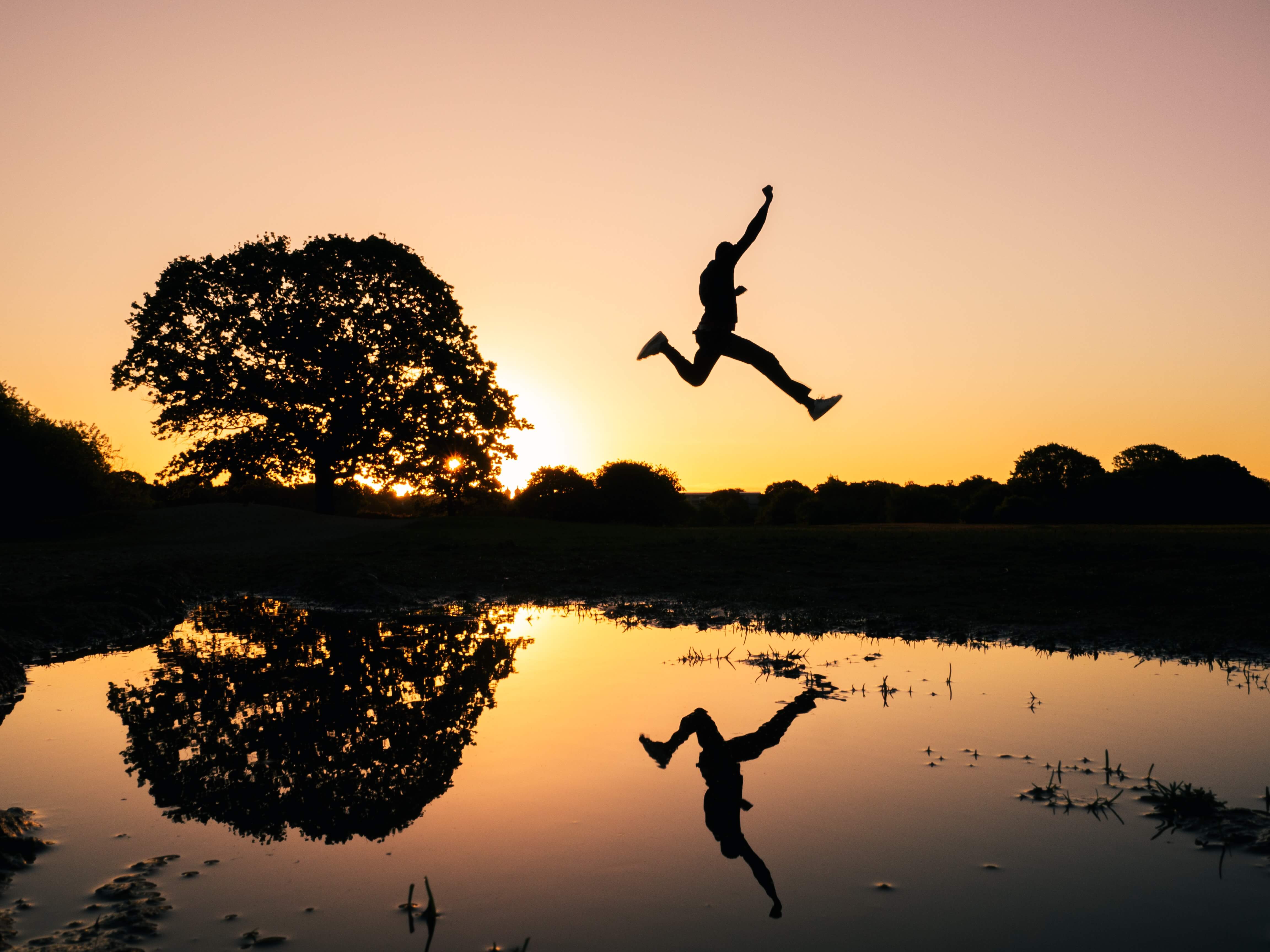 A silhouette of a person jumping over a pond