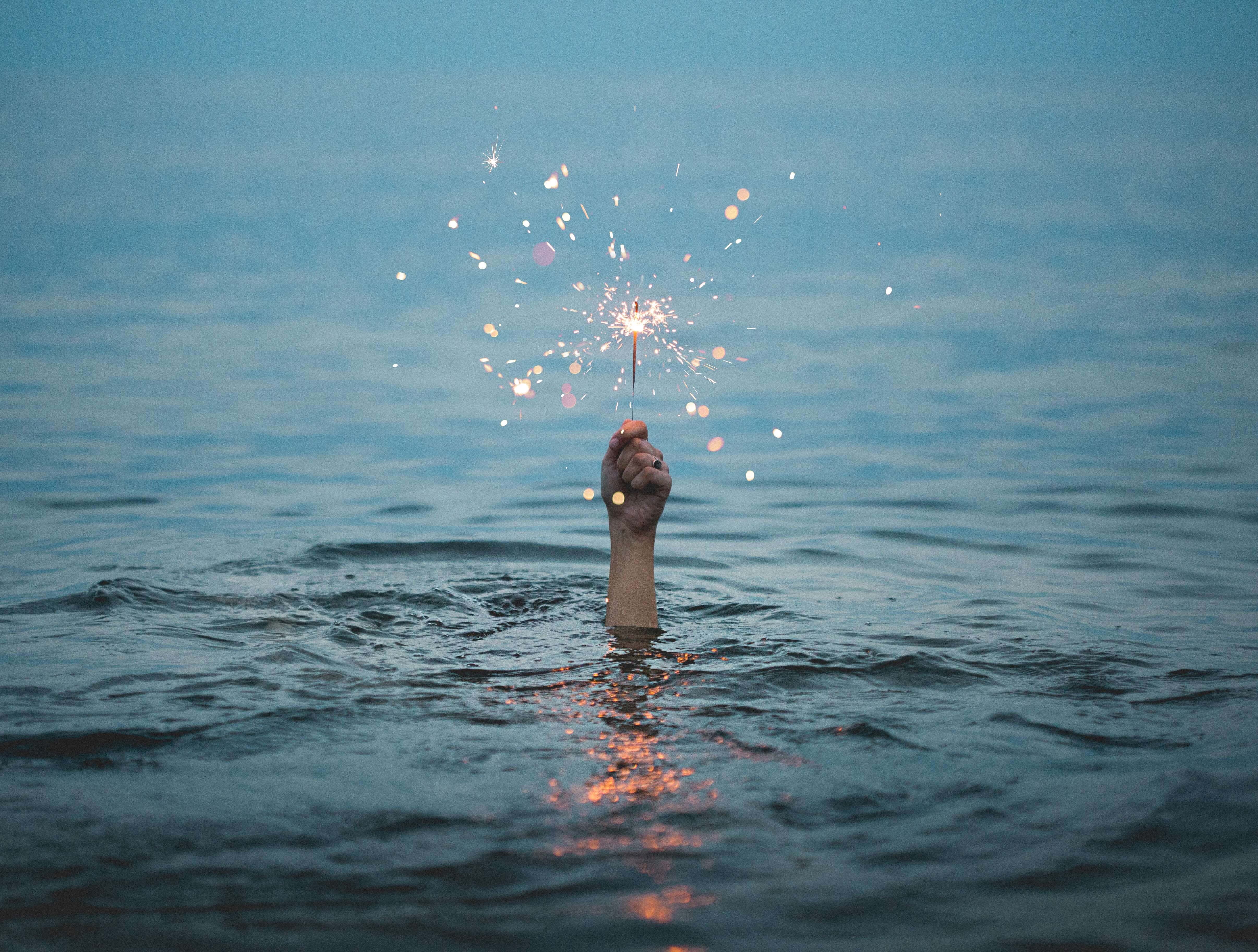 A hand holding a sparkler reaching out of the water