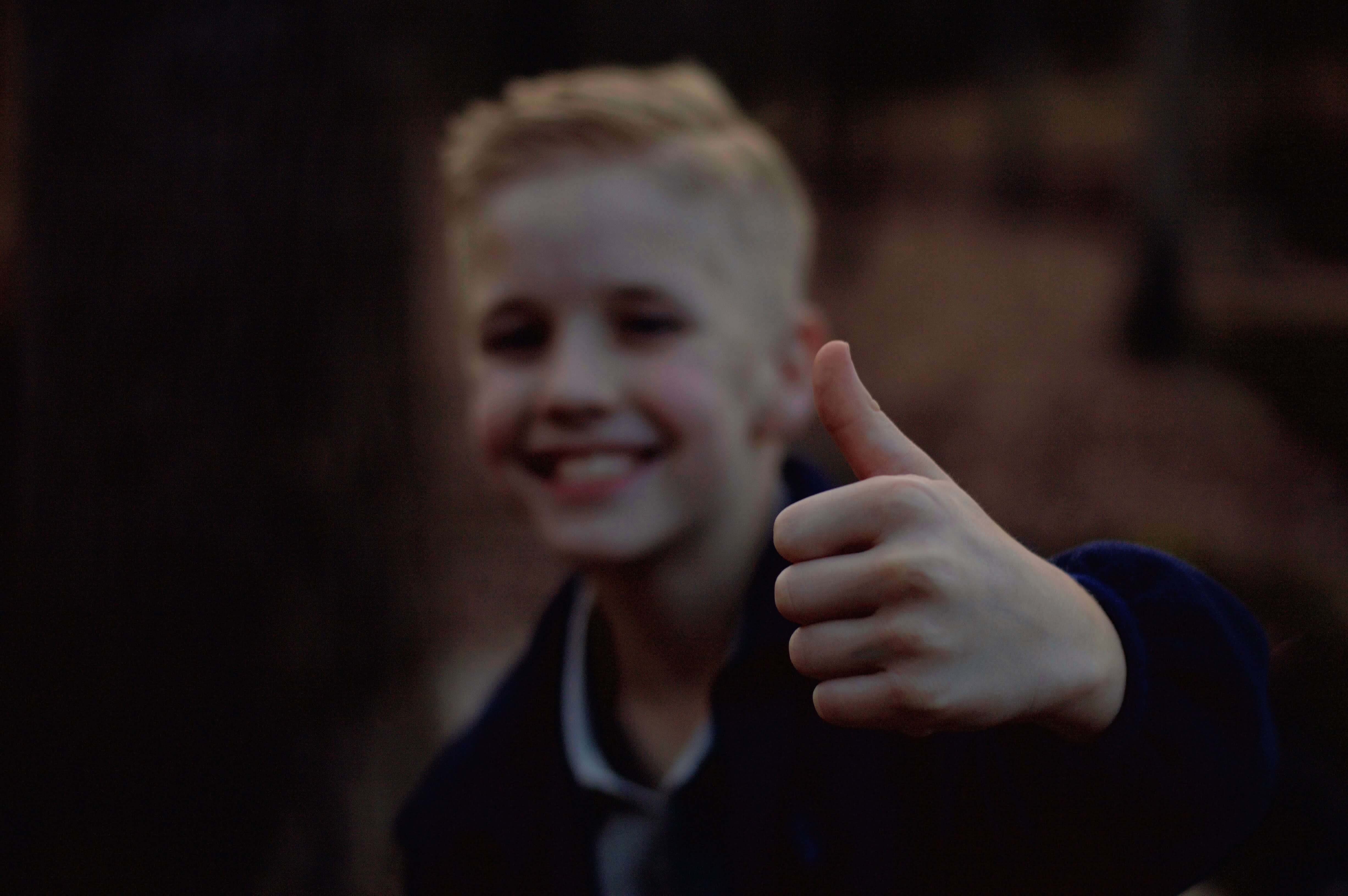 A blond child giving a thumbs up