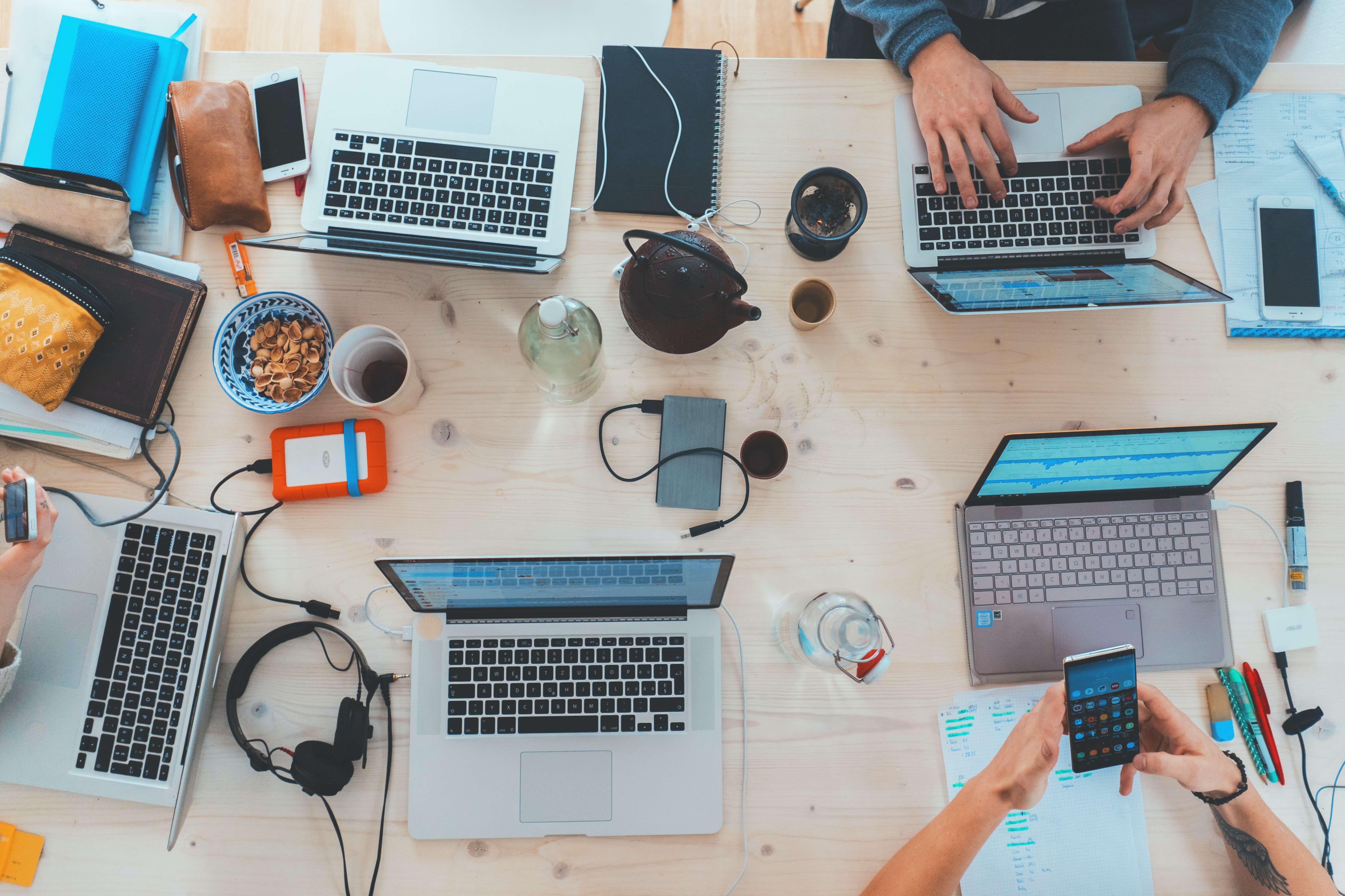 A shot from above of five people working on their laptops at a table littered with various supplies