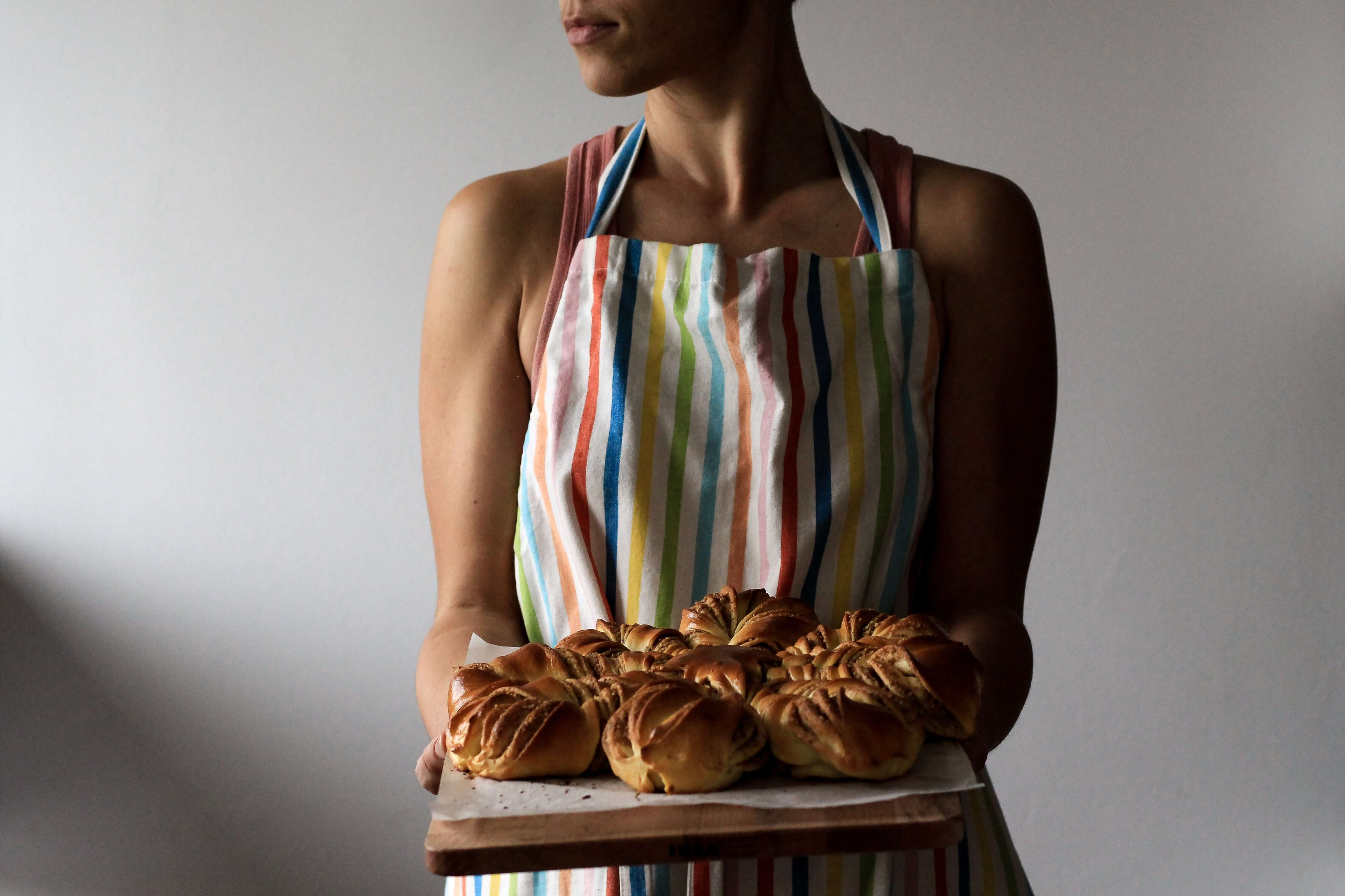 A person wearing a colorful striped apron and holding a tray of pastries