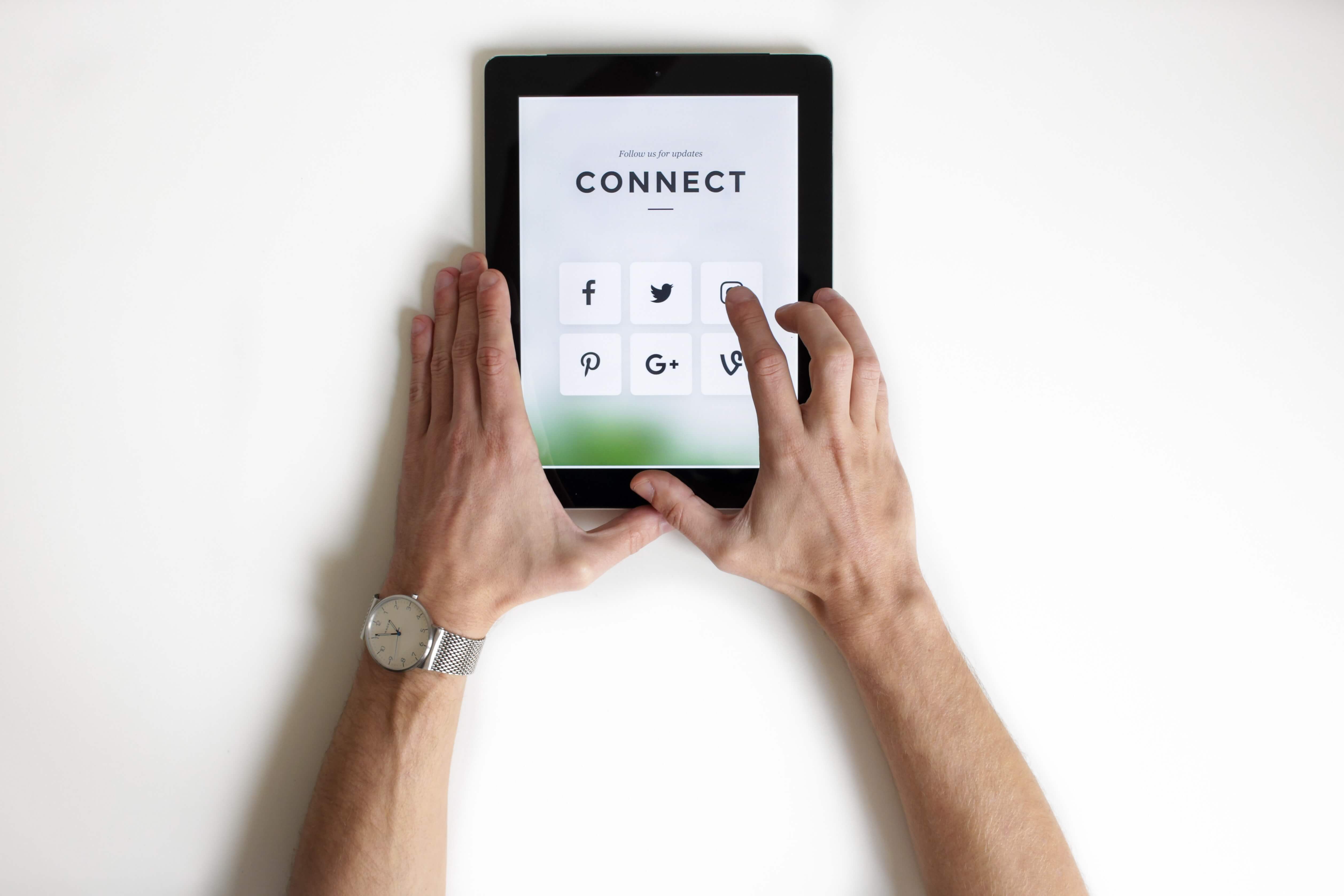 A pair of hands using a tablet displaying the icons for Facebook, Twitter, Instagram, Pinterest, Google Plus, and Vine