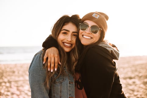 two women hugging and smiling on a beach