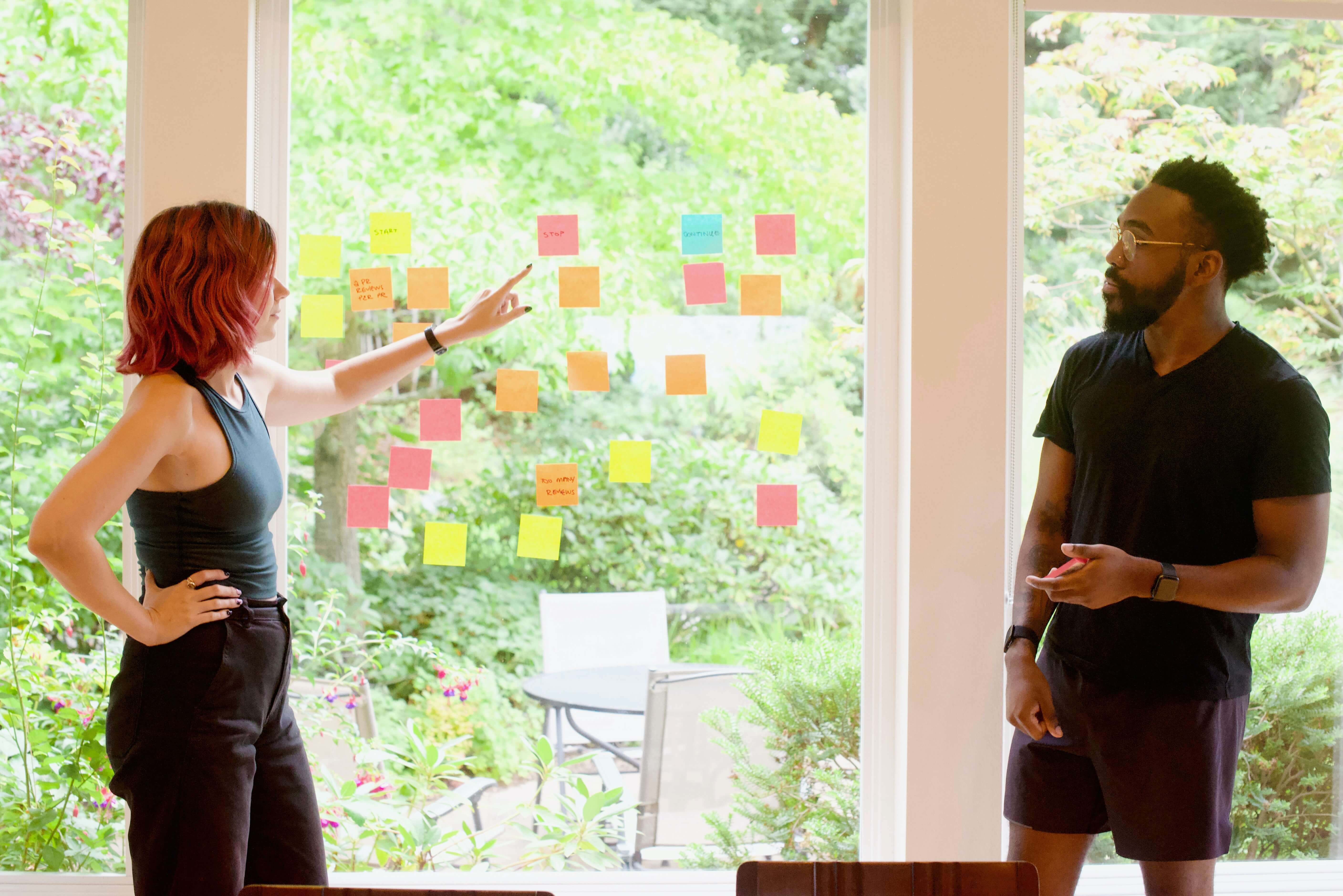 Two people in casual clothing sticking post-it notes on a window in daytime