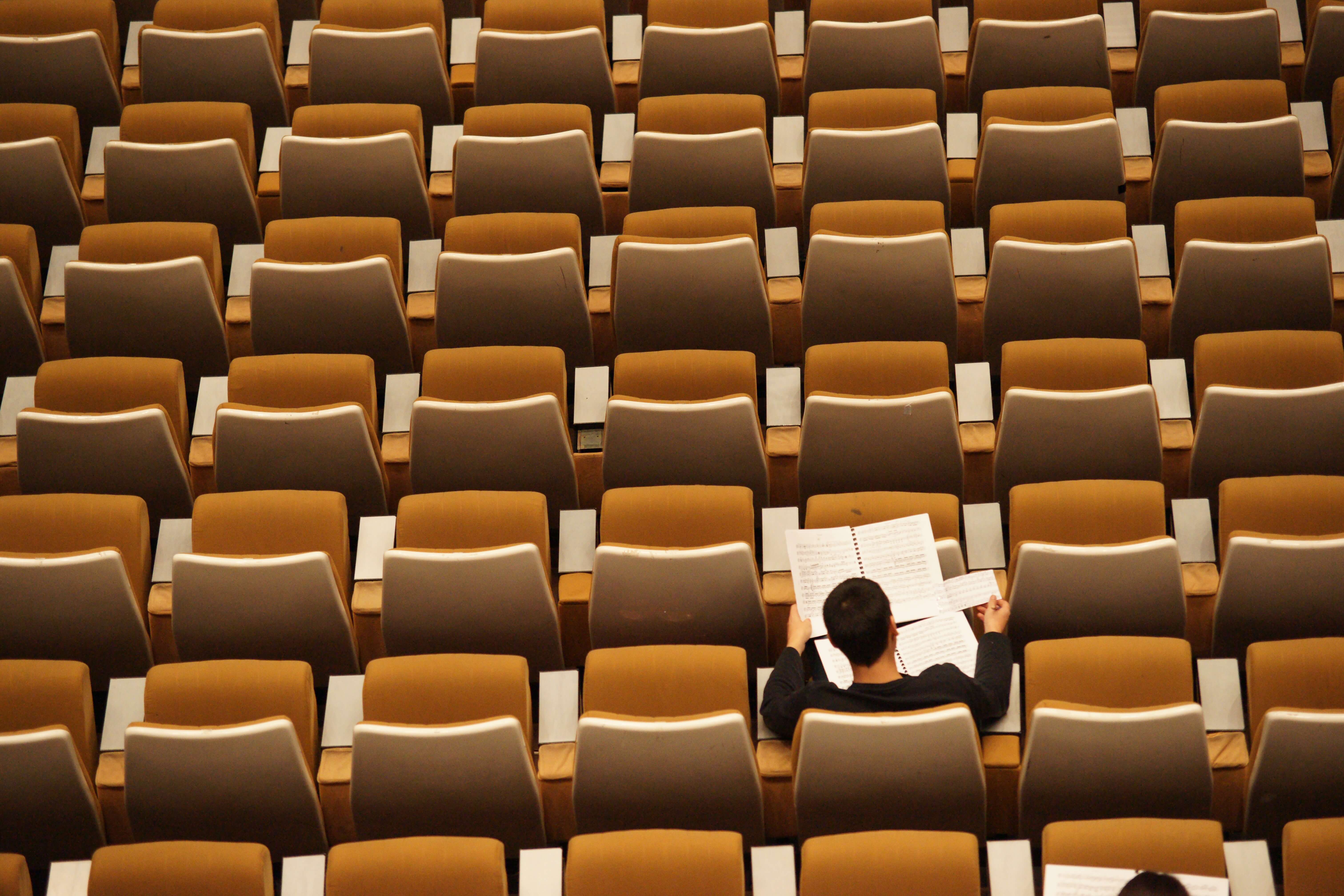 A young adult doing schoolwork in an otherwise empty auditorium