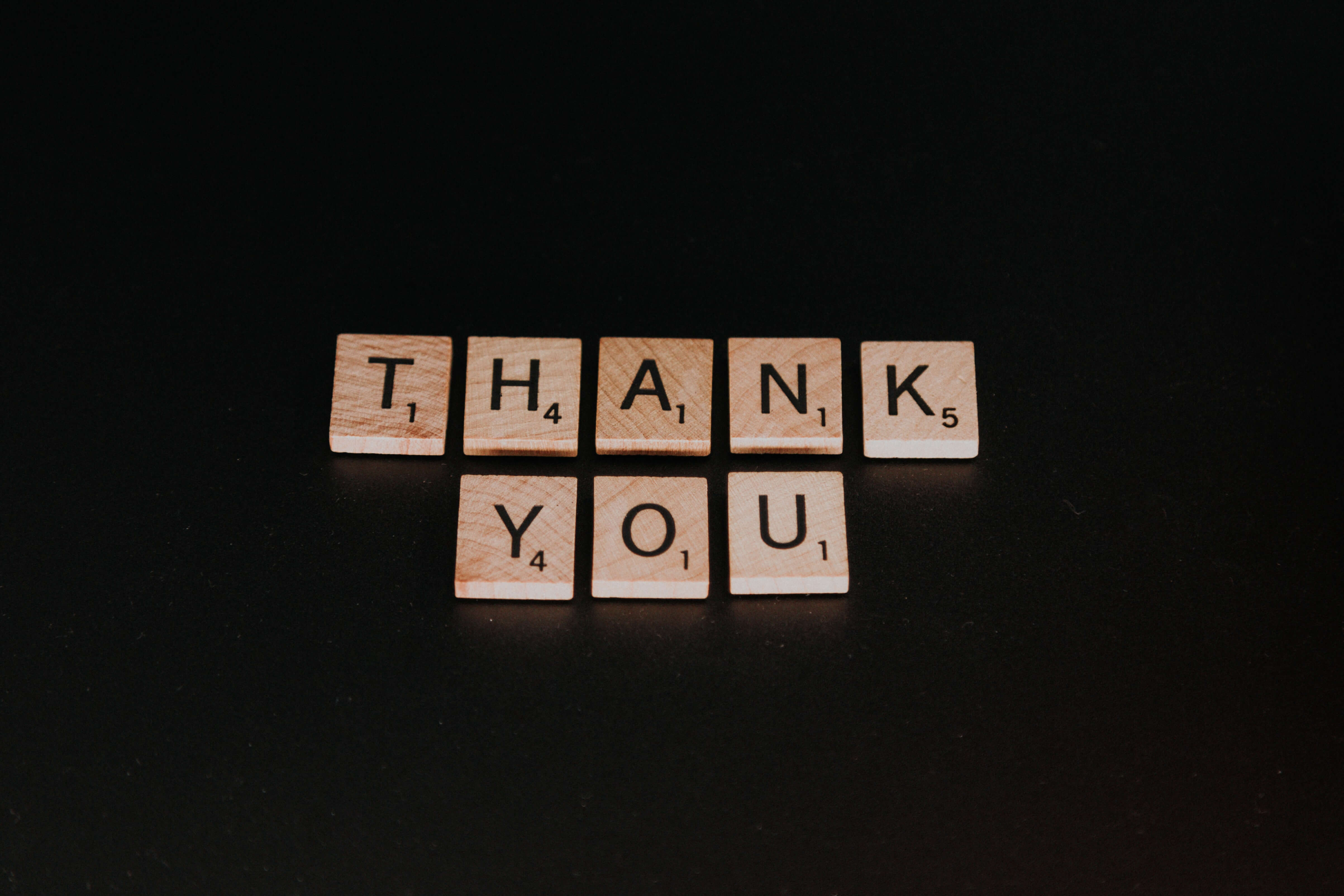 Scrabble tiles spell out "Thank You" on a black background.