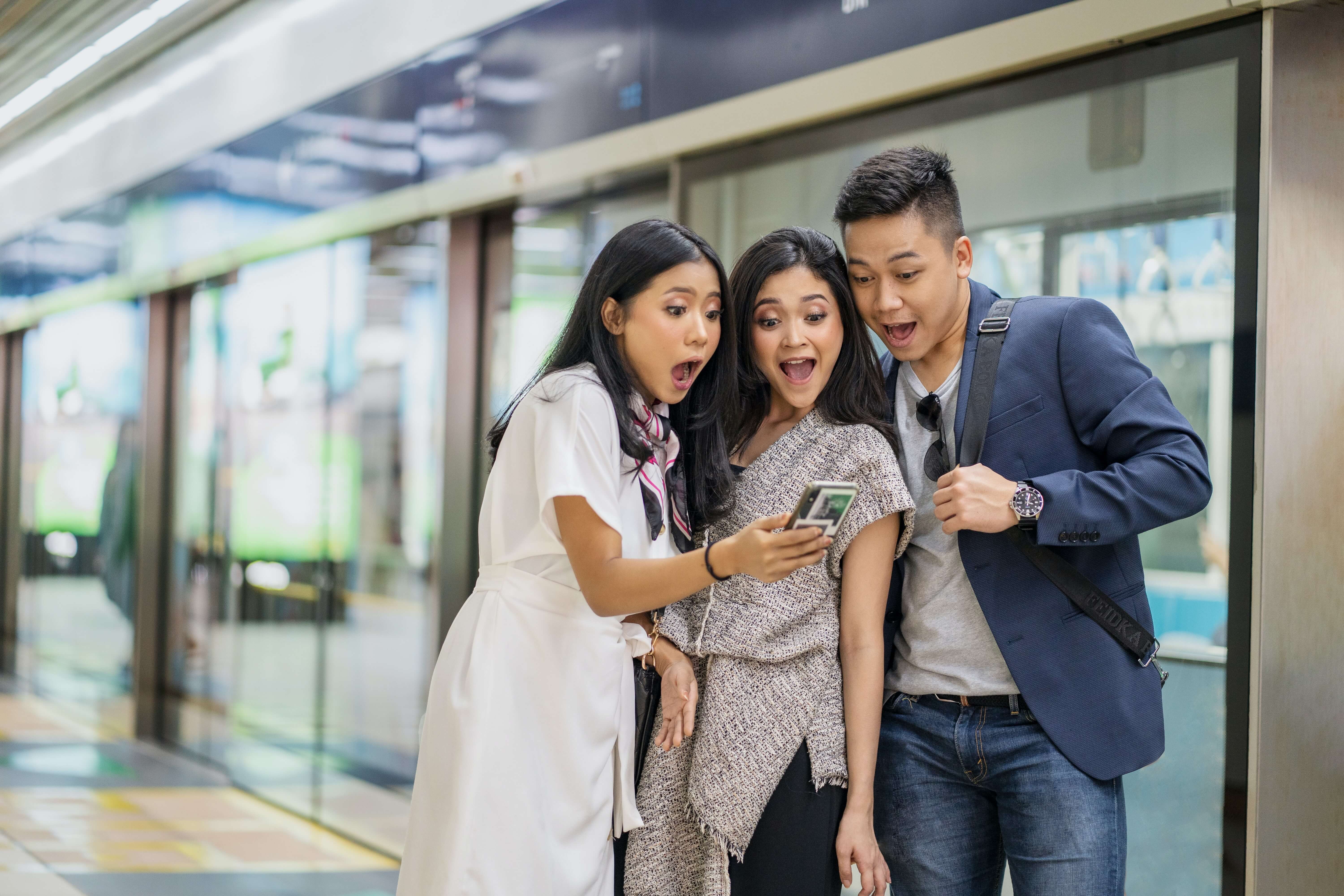 Three people looking at a phone with excited expressions