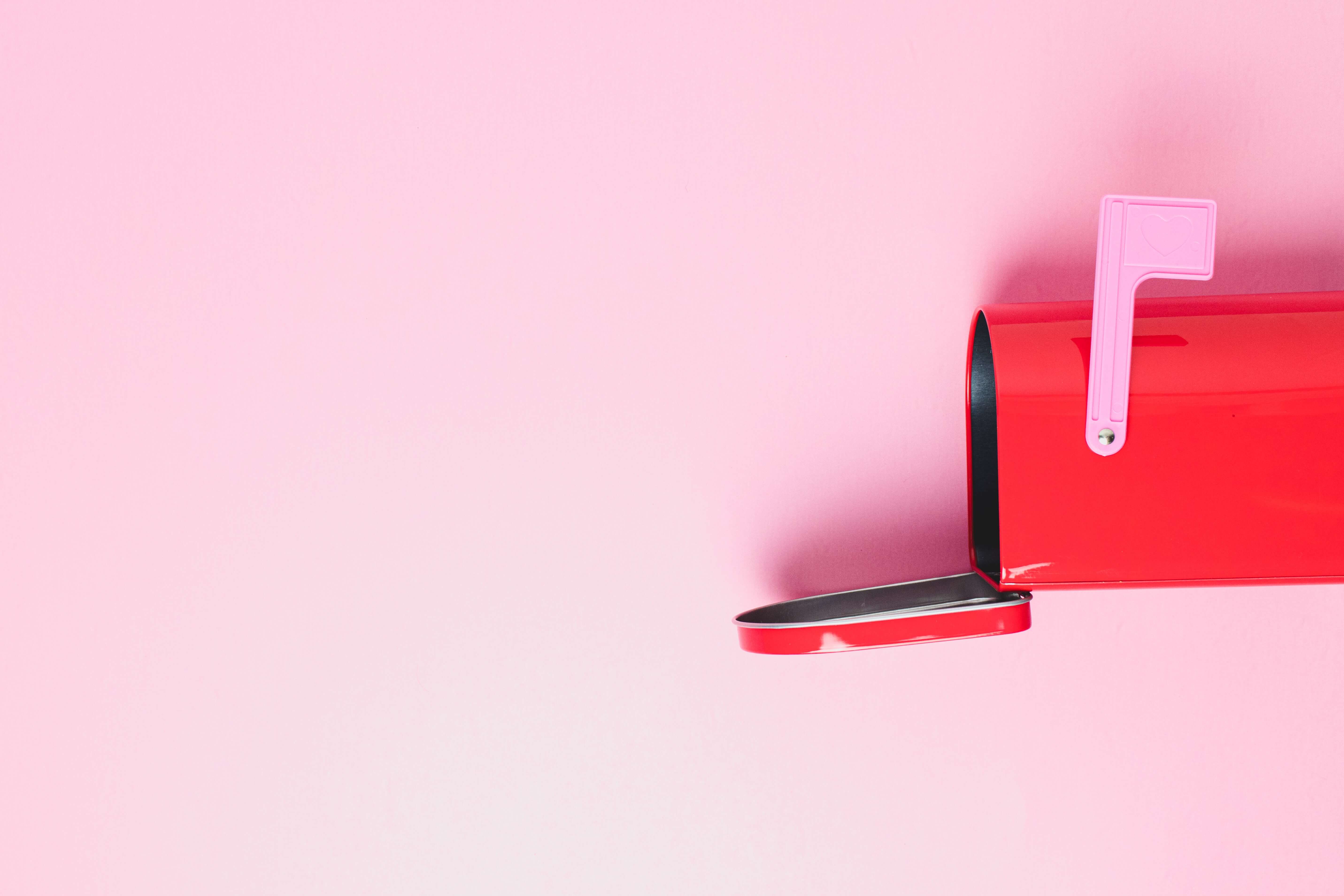 A red mailbox turned to the side and opened against a pink background