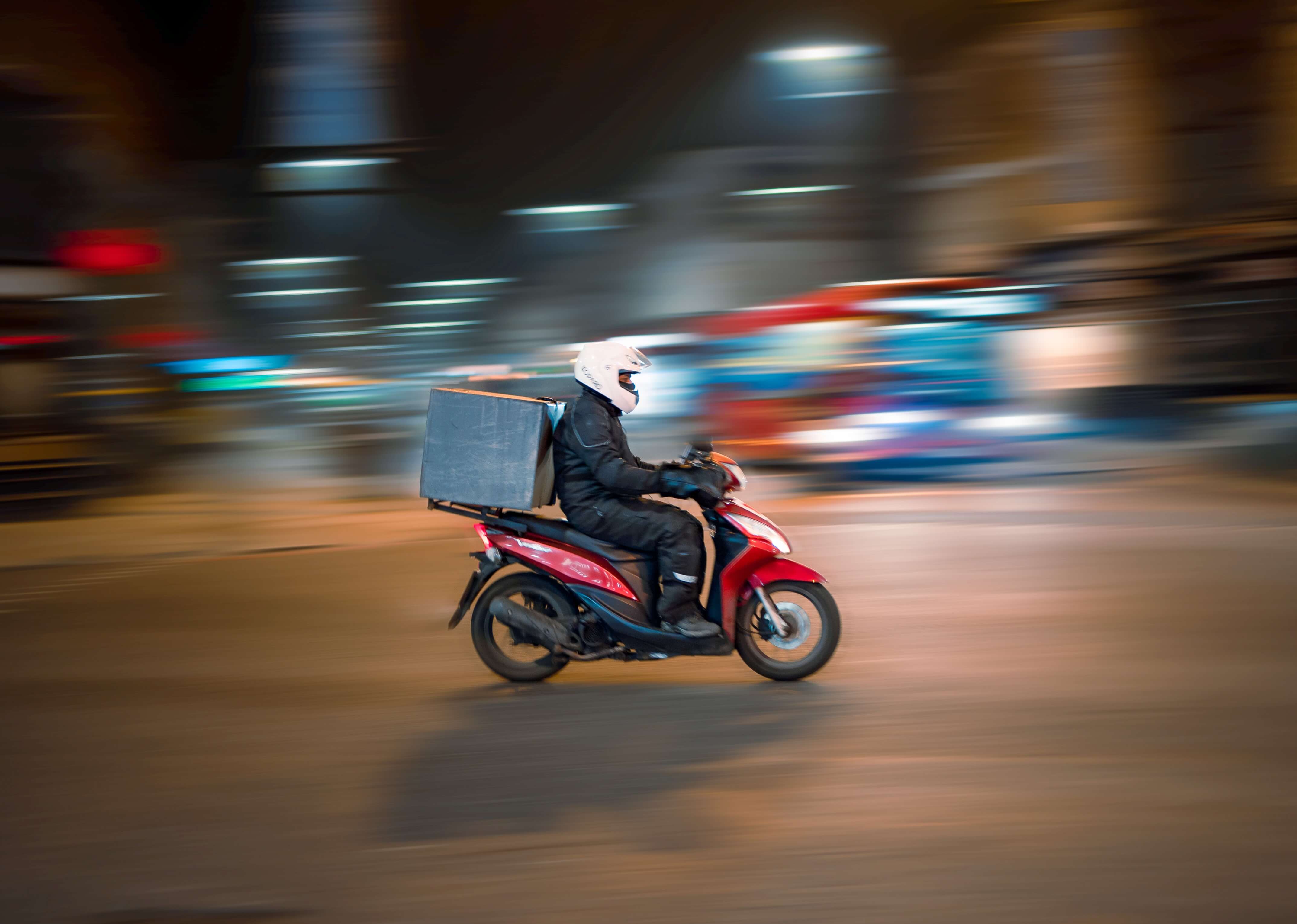 A delivery driver drives a moped while the background whizzes by