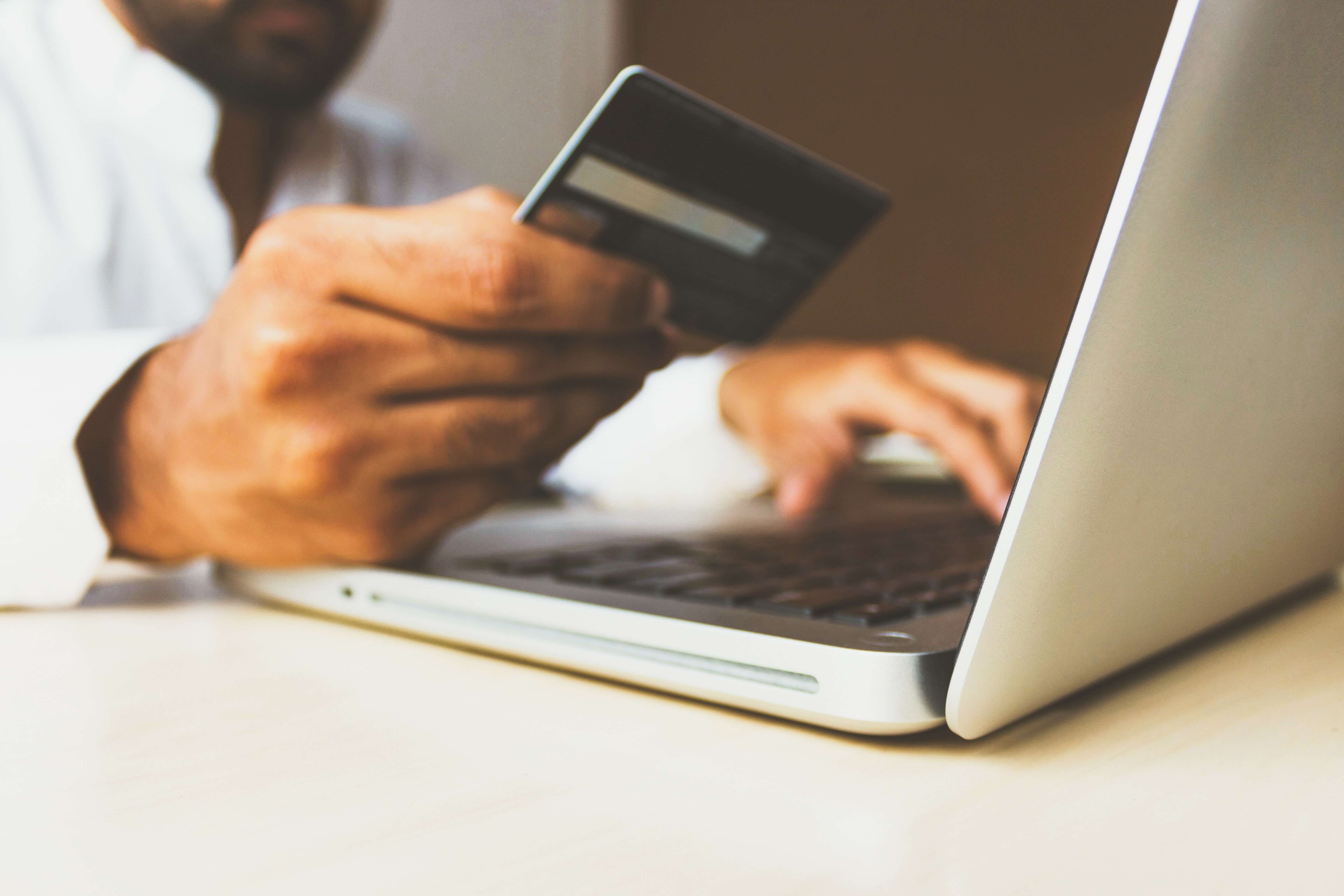 A South Asian man holding a credit card while using a laptop to make an online purchase