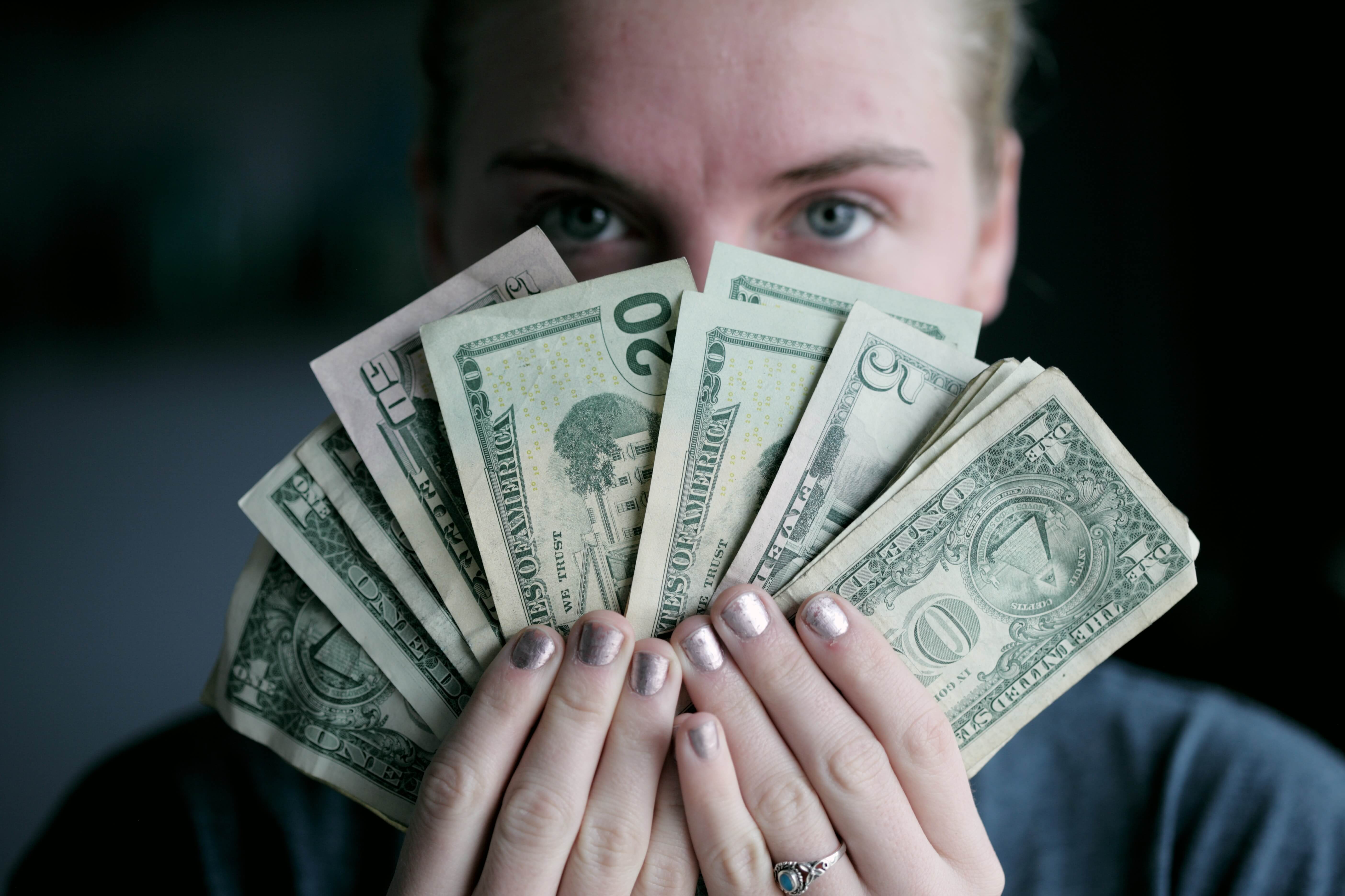 A white woman holding a fan of various US dollar bills in front of her face