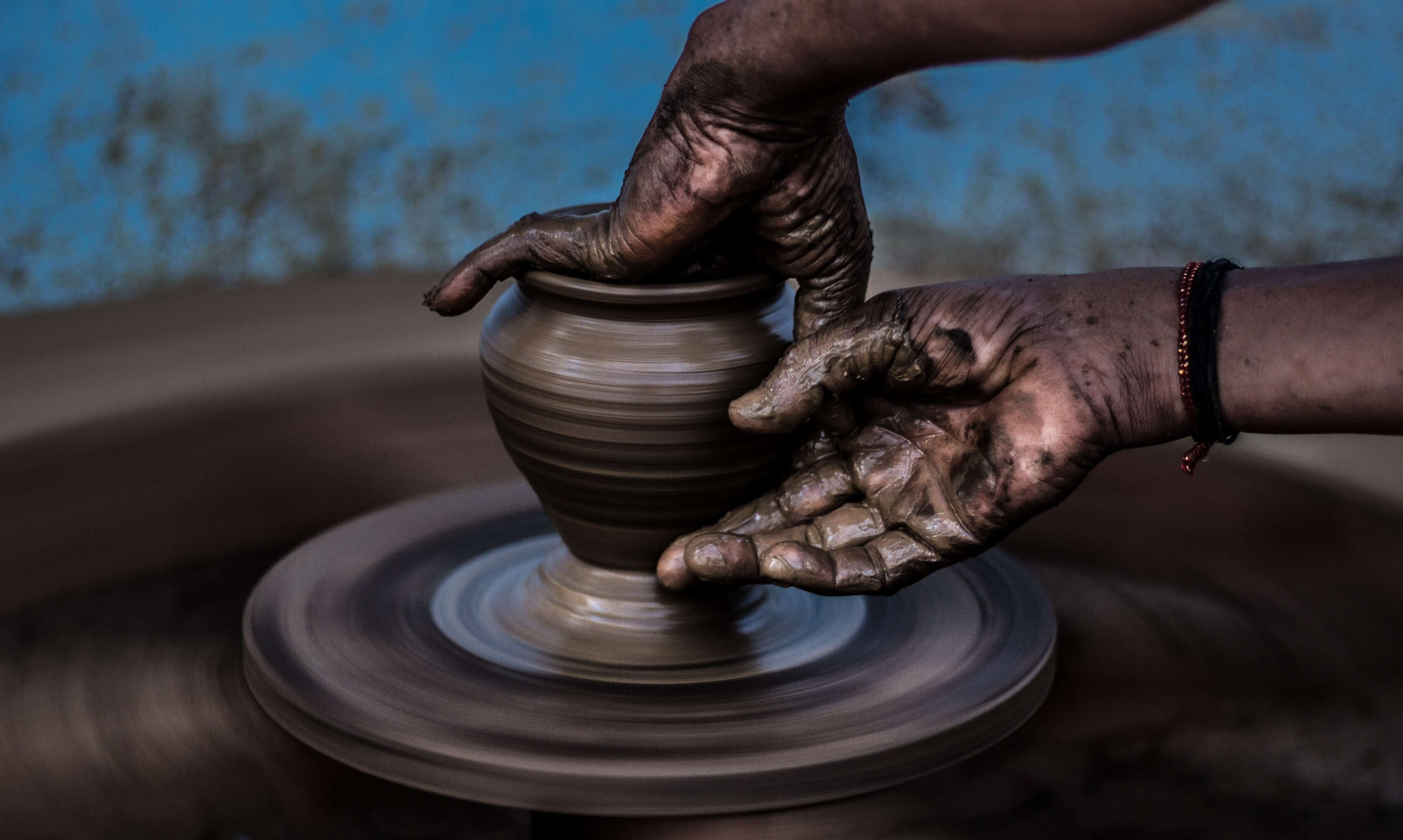 A pair of hands shape a vase on a pottery wheel